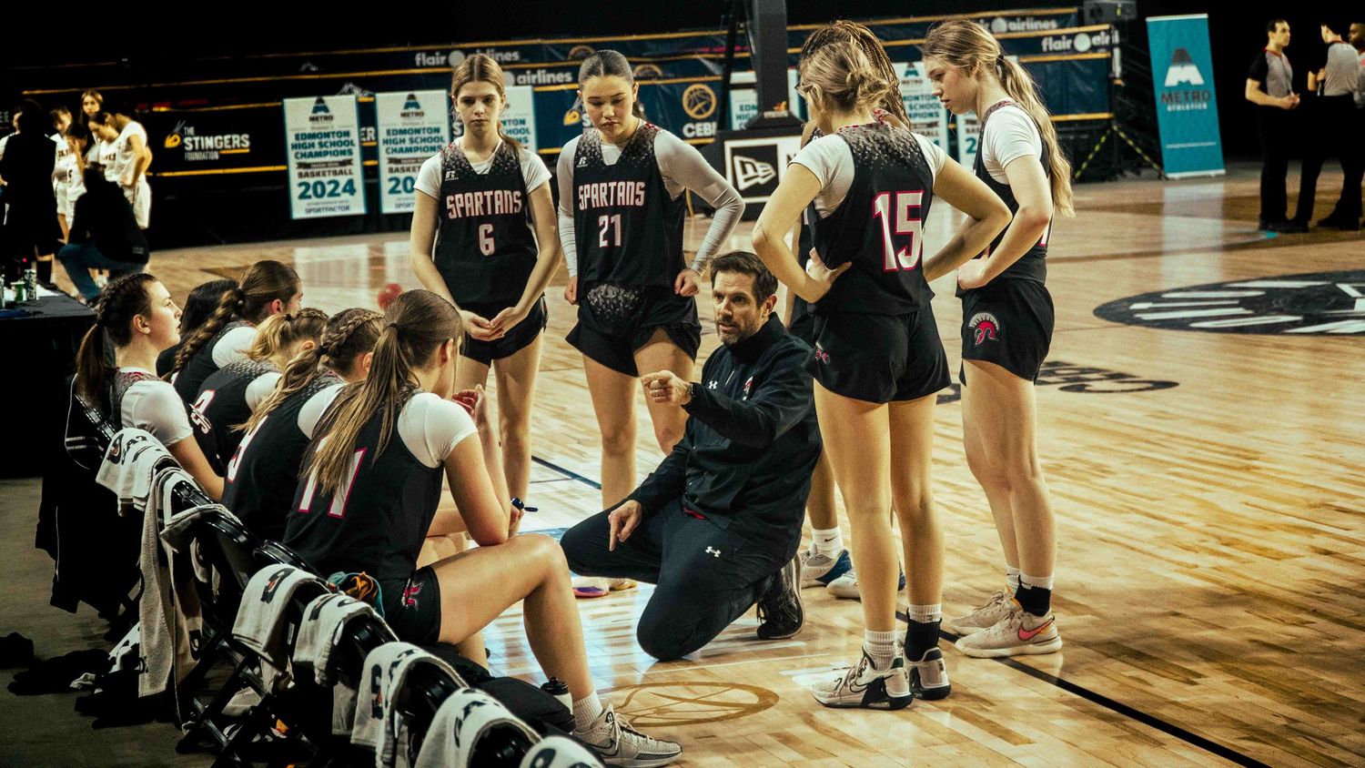 Basketball team huddles on court during game break.