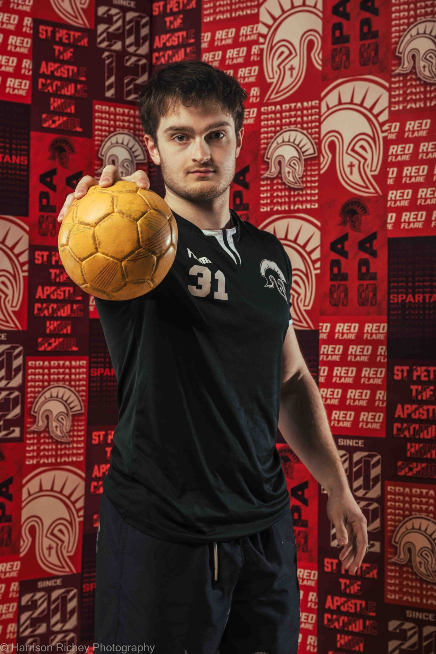 Athlete in black jersey number 31 holds golden handball against red patterned background.