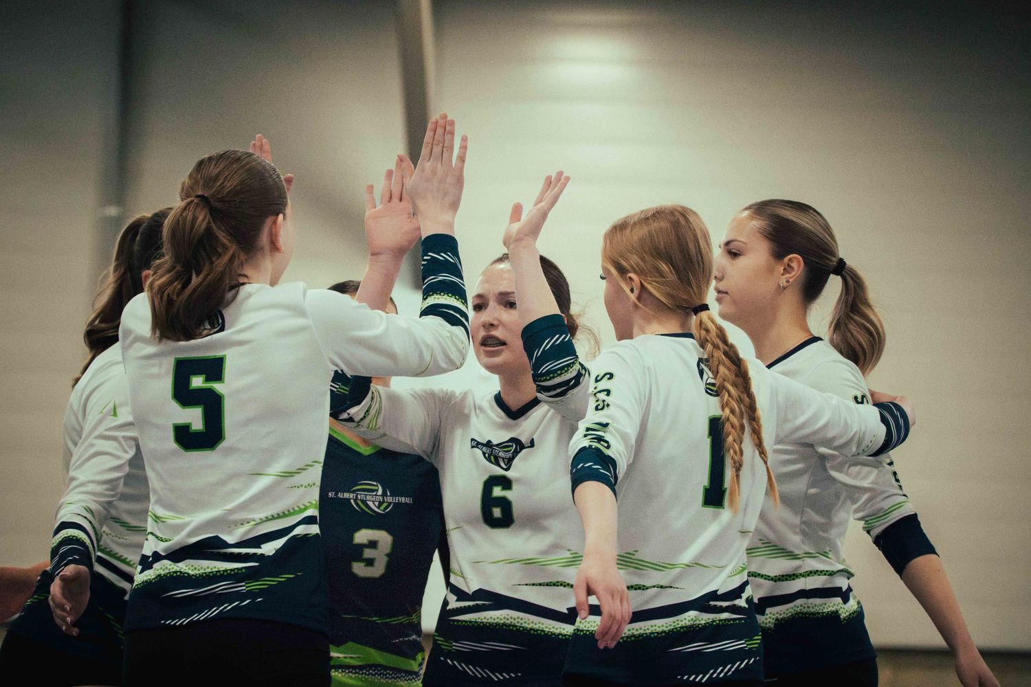 Volleyball players huddle together giving high fives in green and white uniforms.