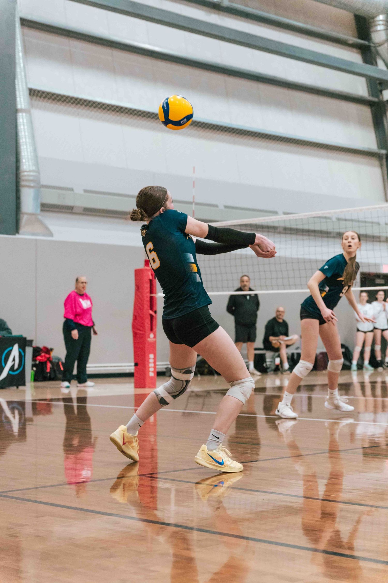 Volleyball player in dark uniform stretches to hit yellow ball during indoor game.