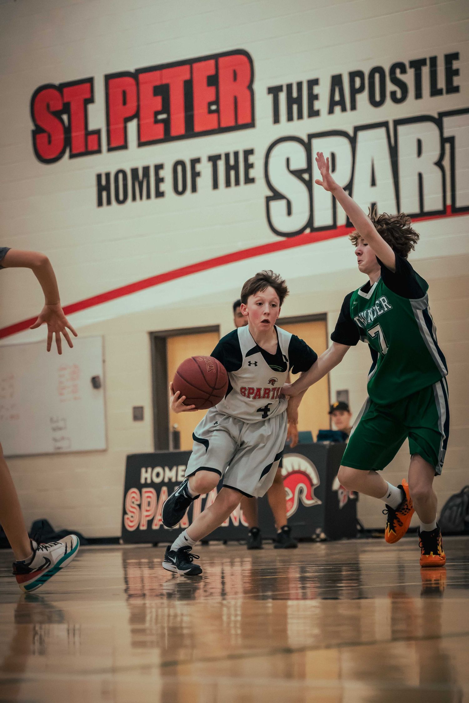 Players in green and gray jerseys stretch and dive for the ball during a youth basketball game.