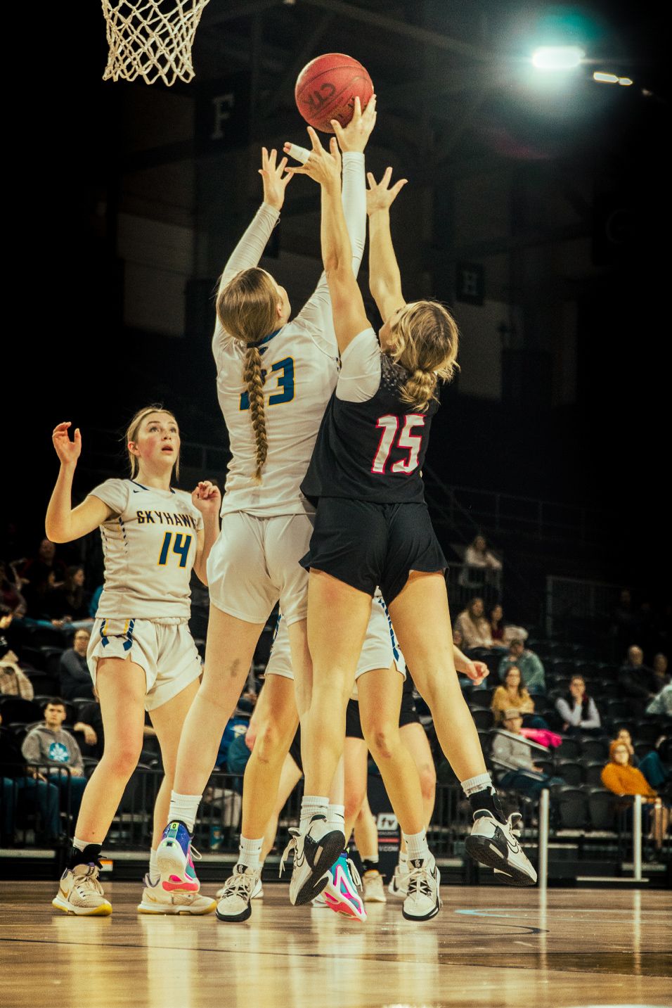 Basketball players jumping for the ball during intense game action under the hoop.