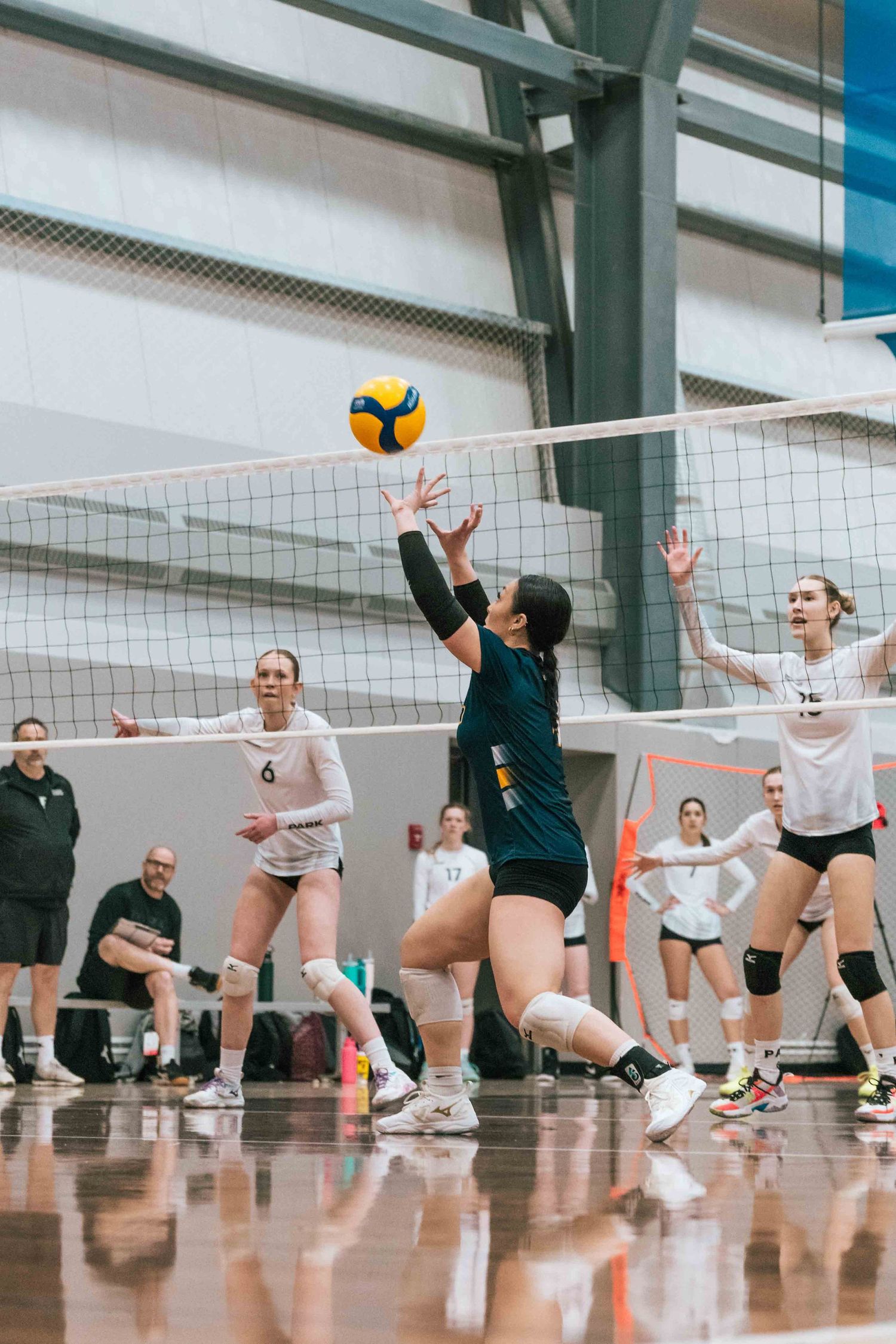 Athletes compete at net during competitive indoor volleyball match on polished court.