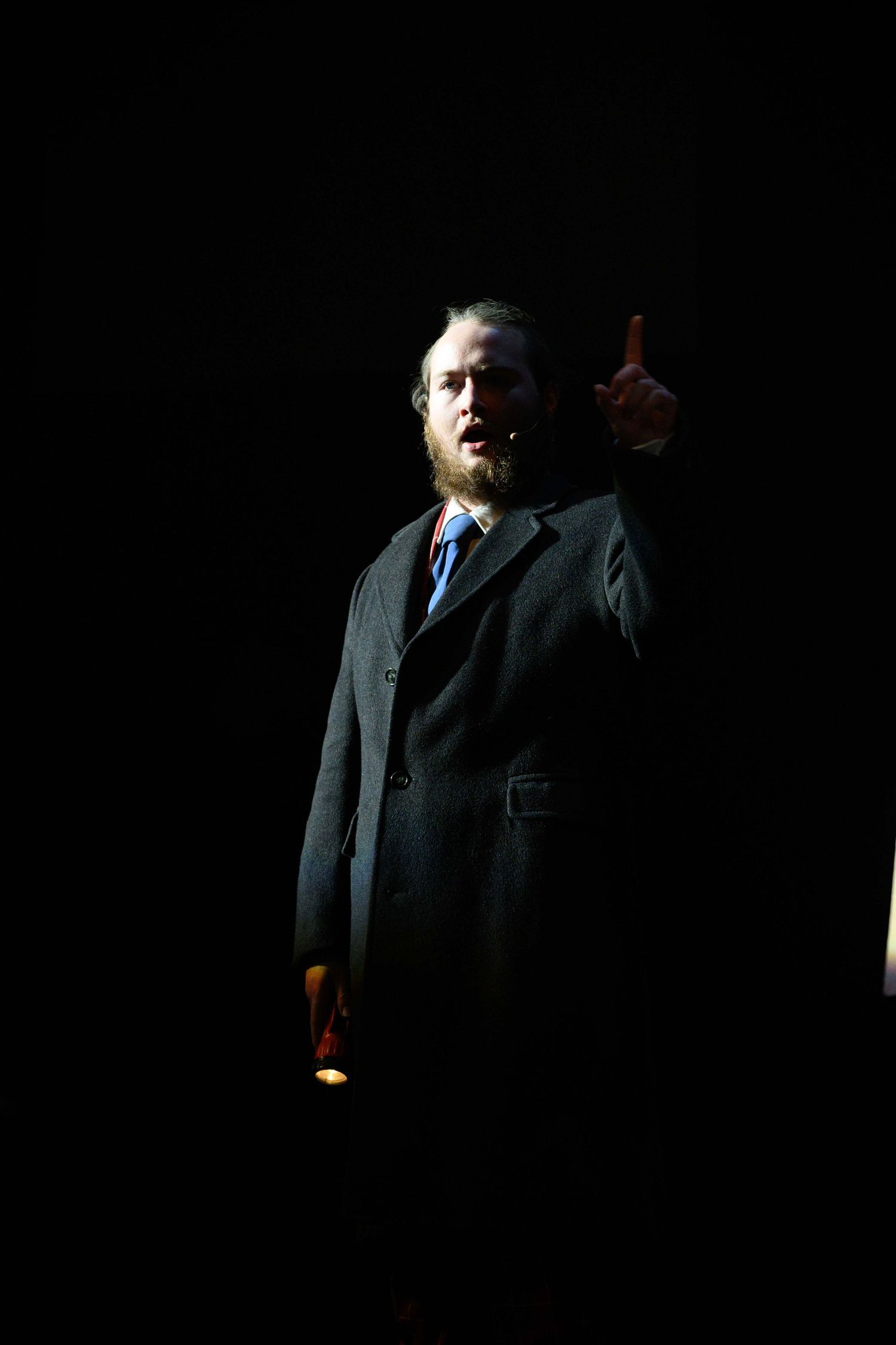 Dramatic silhouette of performers in dark suits against black background.