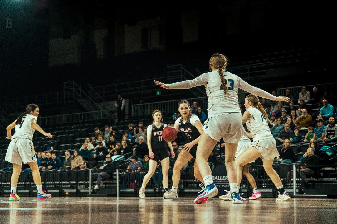 Basketball players competing in an indoor game with defensive positioning on the court.