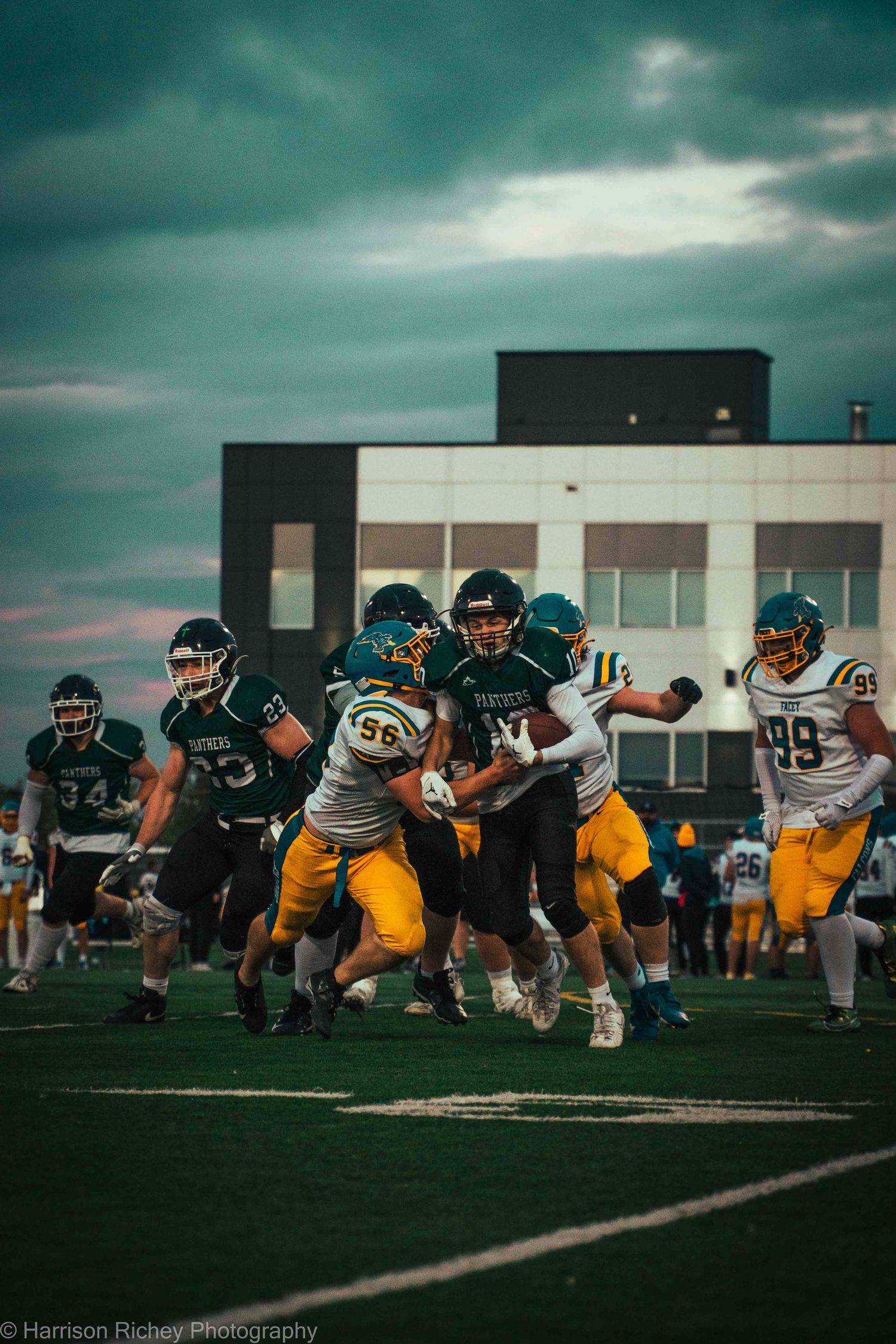 Two football teams battle for position during a dramatic evening game under moody skies.