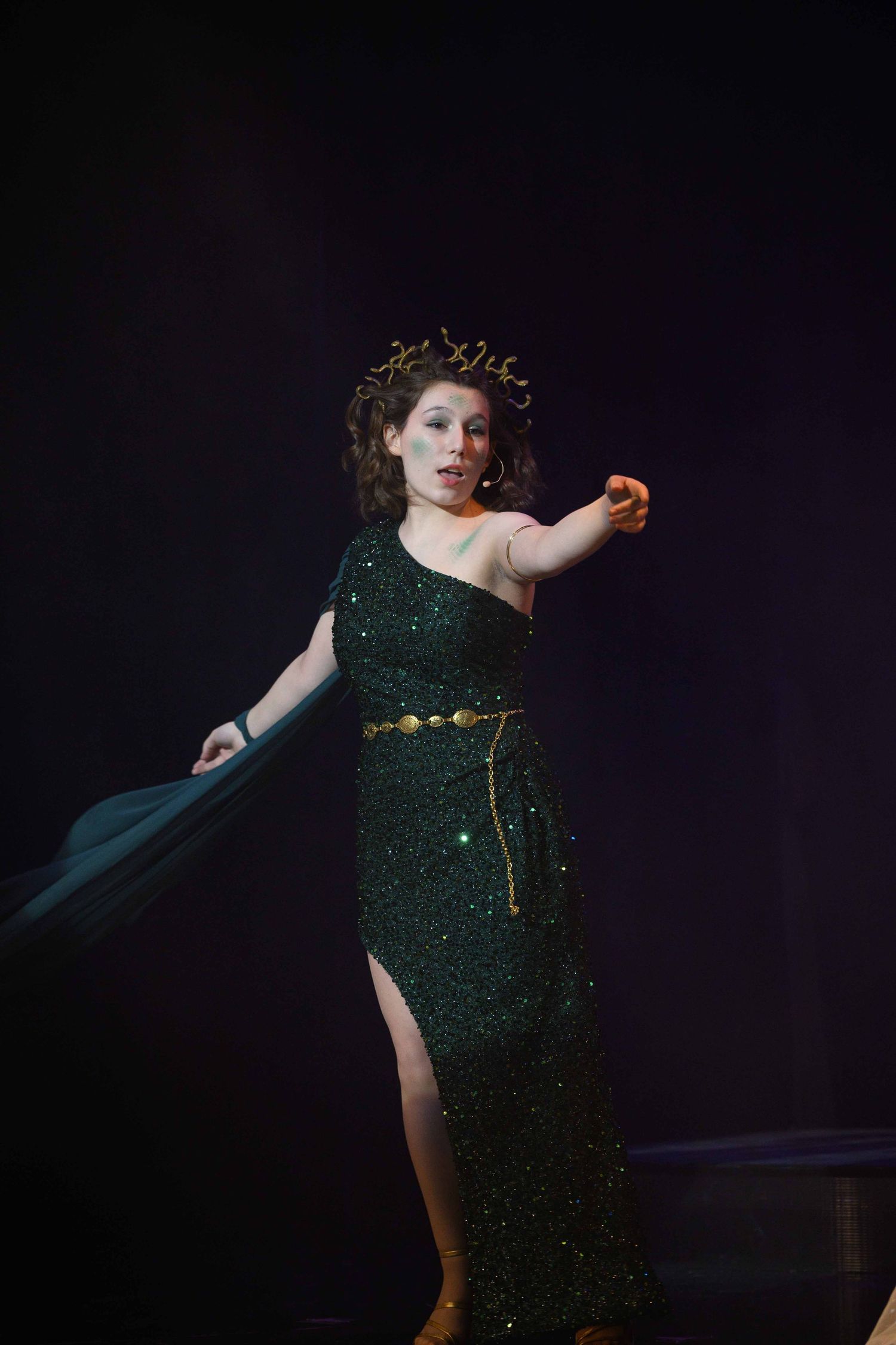 Performer in a sparkling green dress with dramatic poses against dark background.