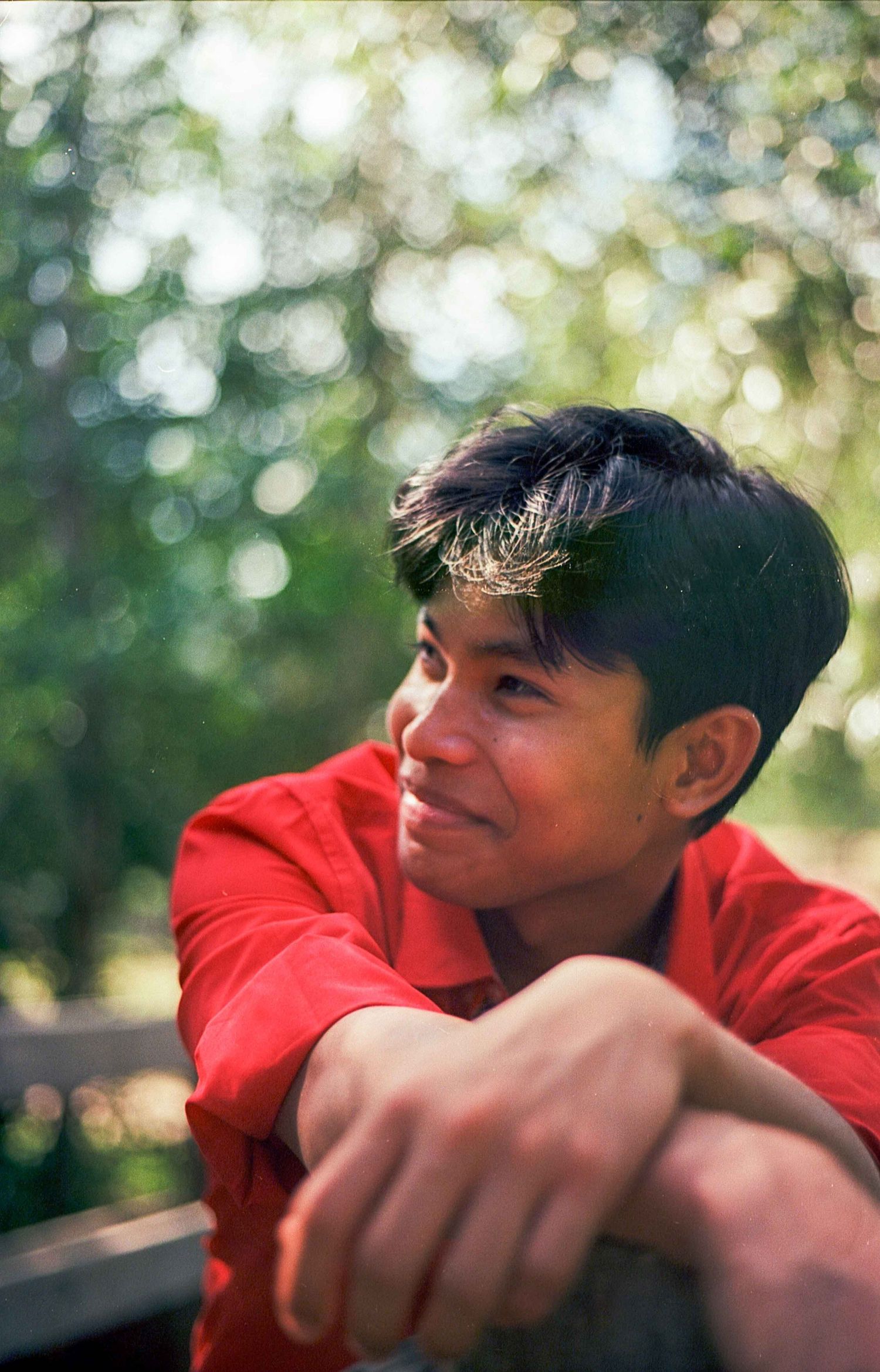 A candid outdoor portrait with soft bokeh lighting and natural greenery in the background.