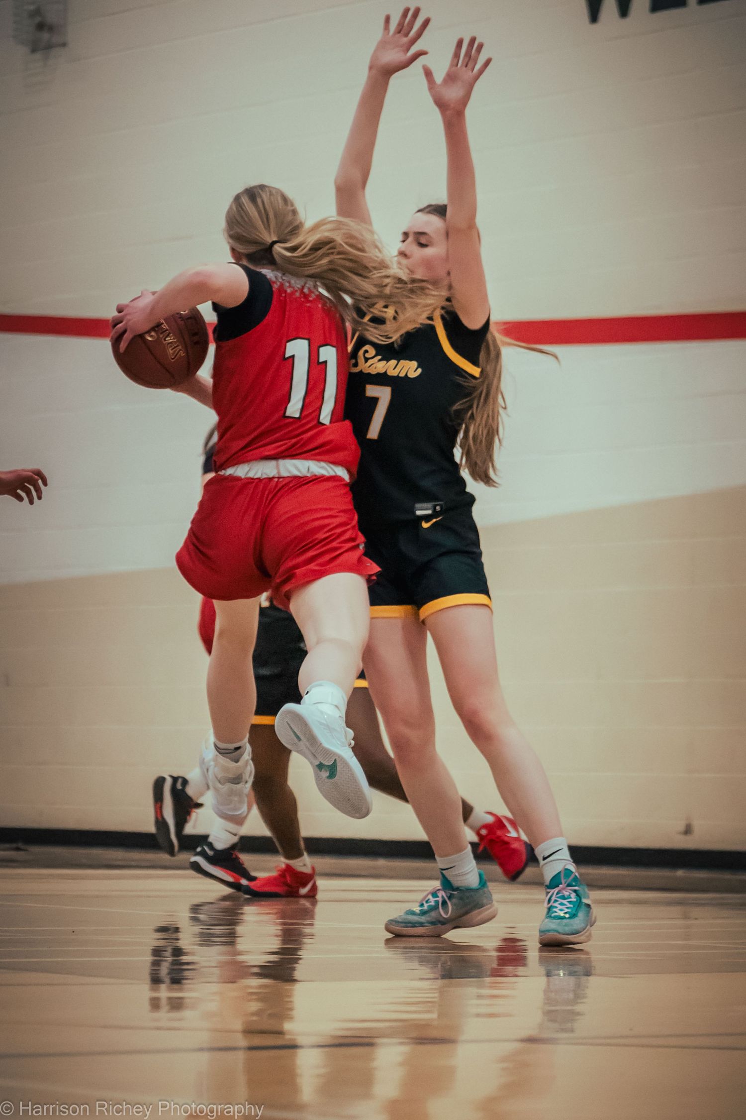 Basketball players in red and black uniforms move swiftly across a shiny gymnasium floor.