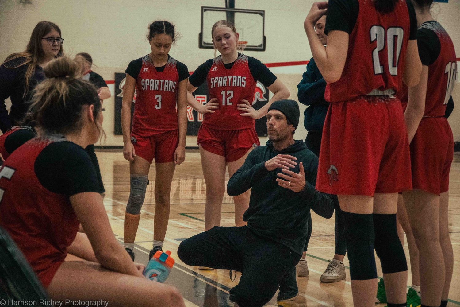 Indoor sports team huddles during practice session in gymnasium.