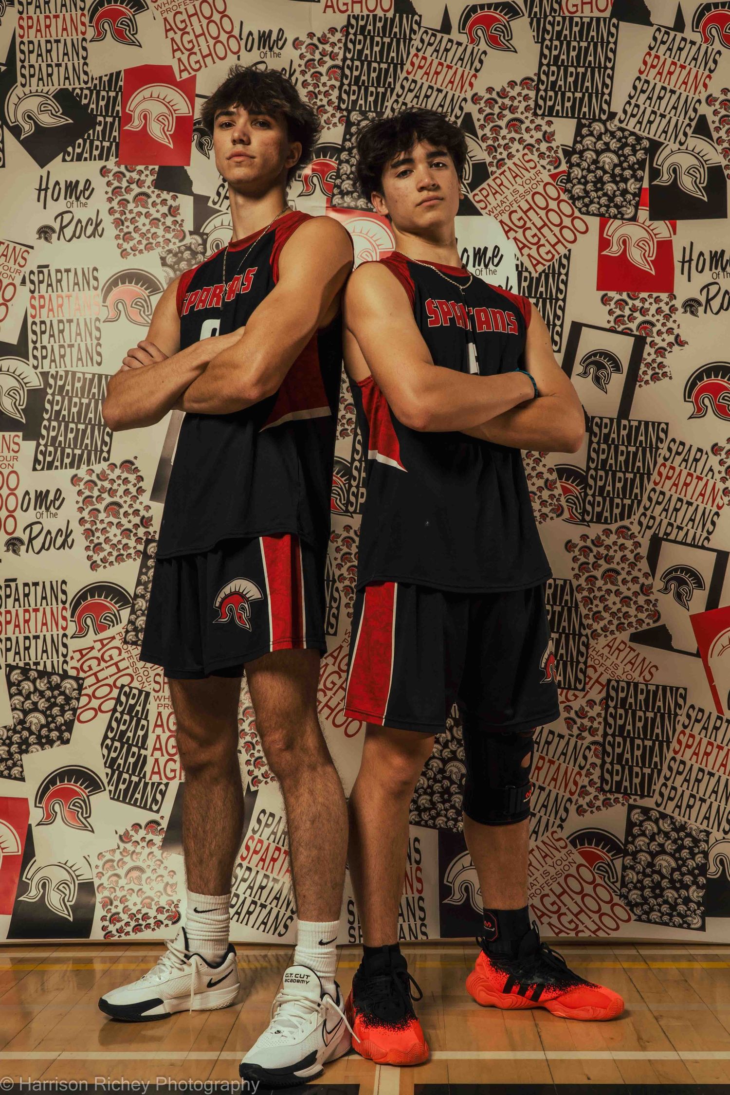 Athletes in black and red uniforms pose against wall decorated with team logos and graphics.