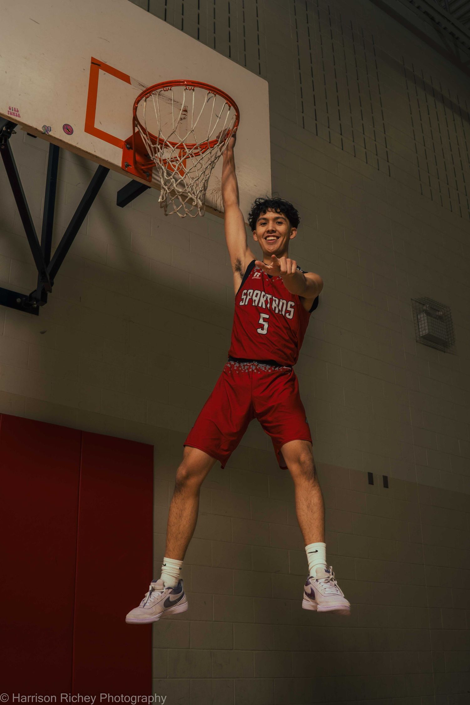 Player executes athletic dunk while wearing red basketball uniform in gymnasium.