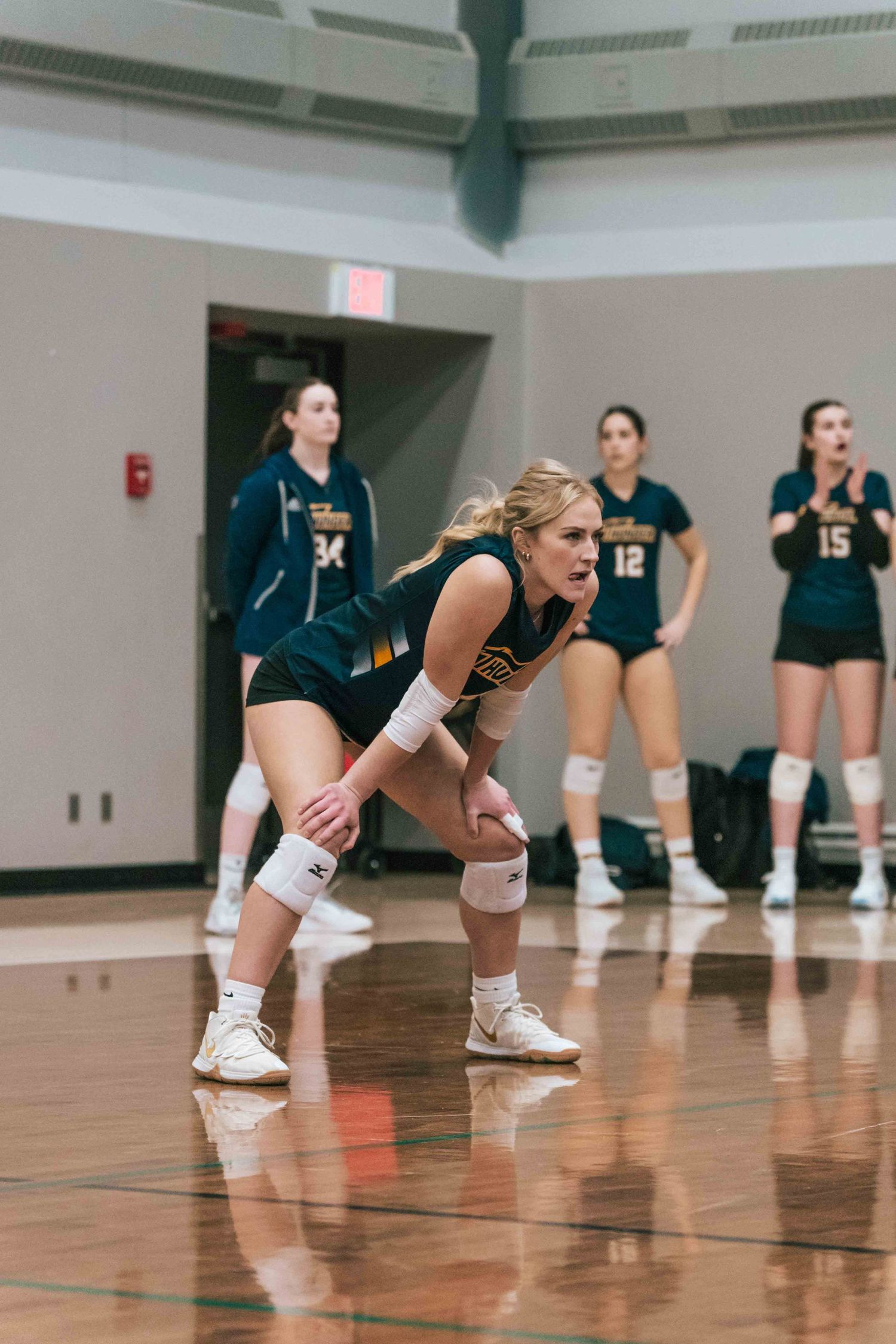 volleyball players in ready position during indoor match with teammates lined up.