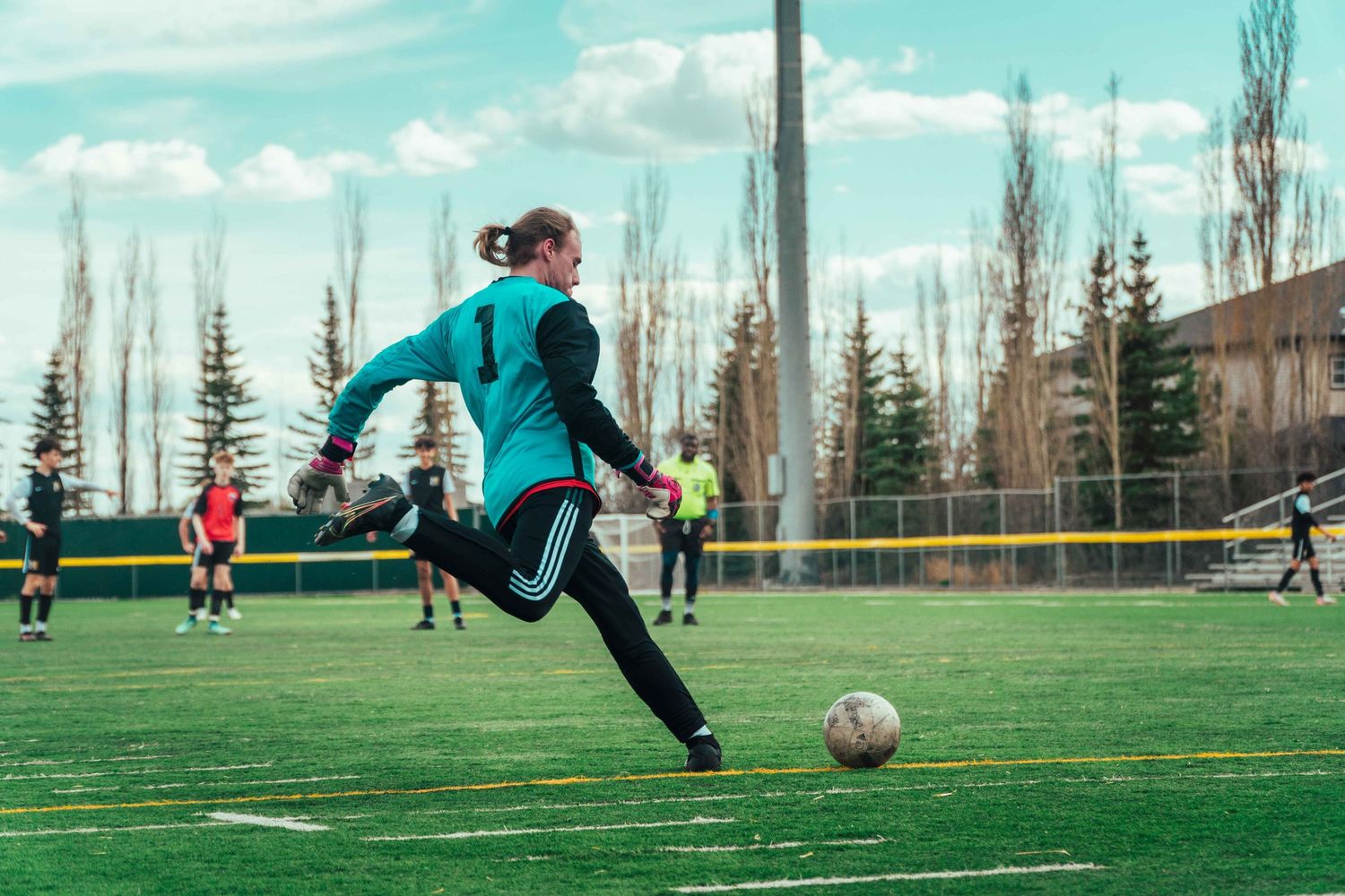 Soccer player in teal jersey prepares to kick ball on outdoor field.