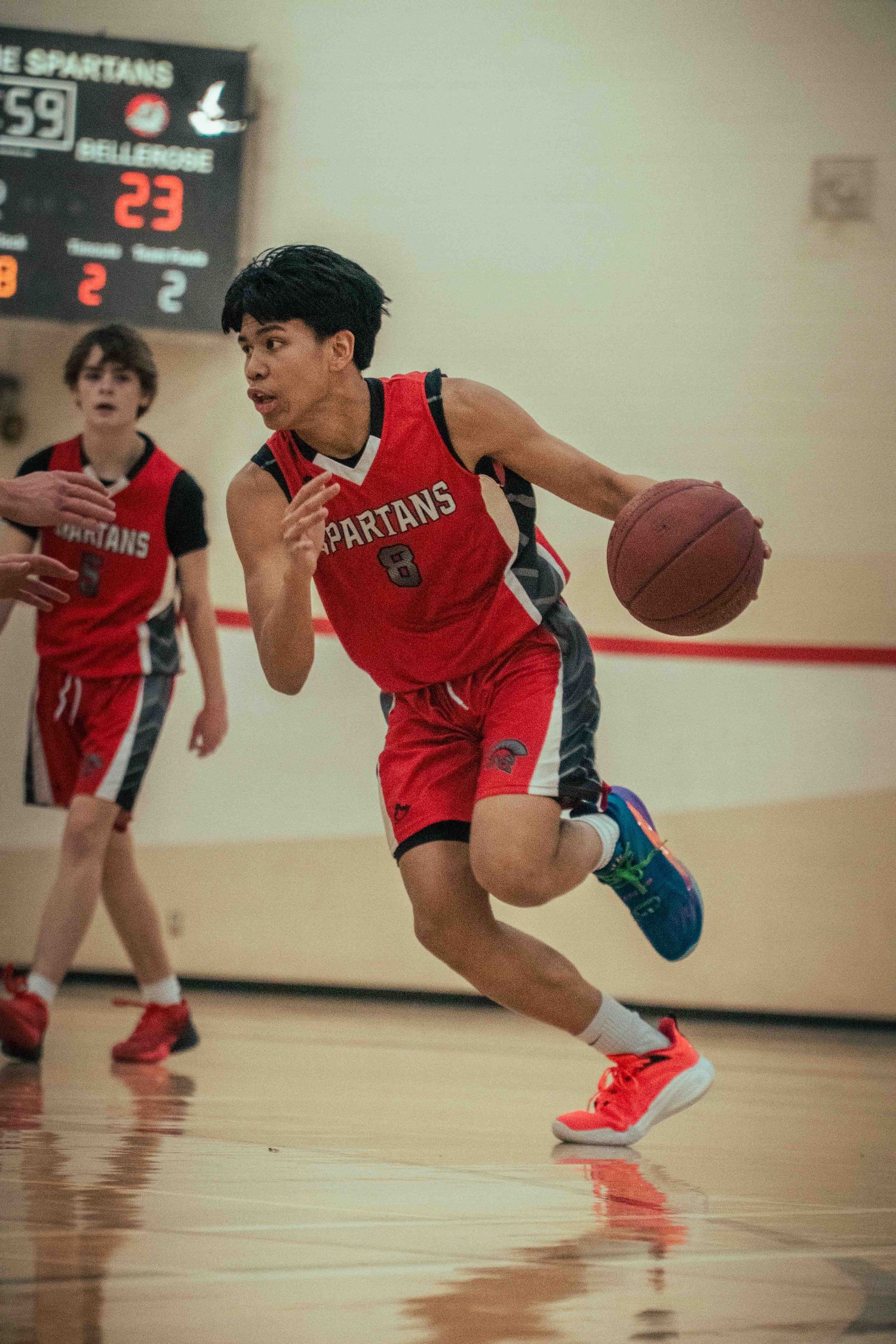 Basketball player in red Spartans uniform dribbles across court during fast break play.