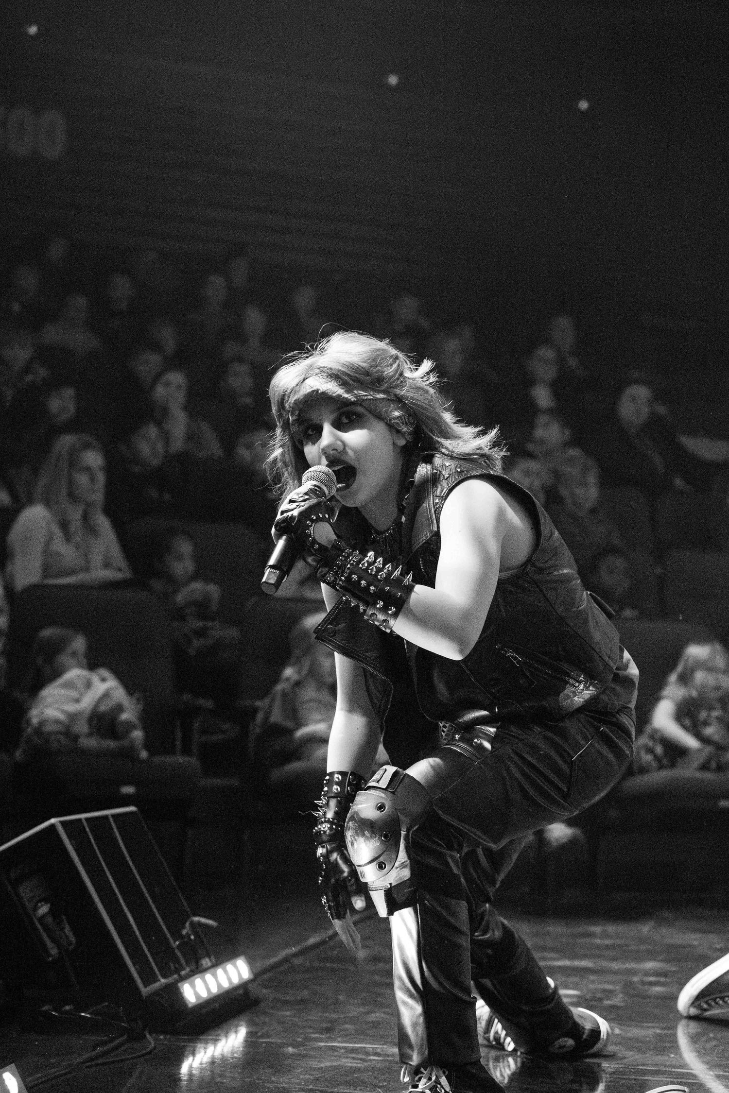 Dramatic black and white performance shot of dancers on stage with audience visible.