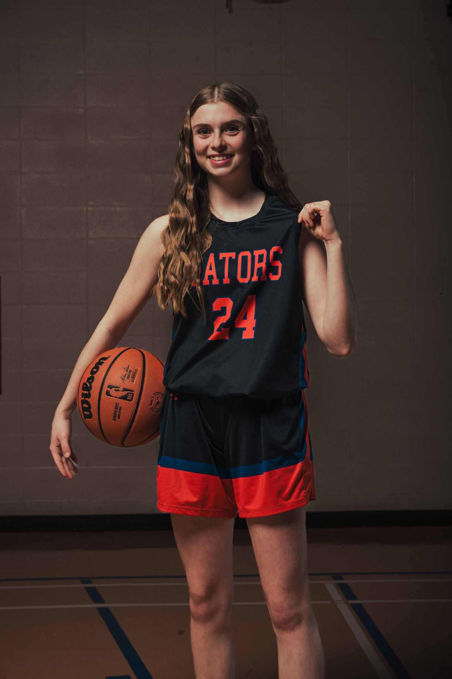 Basketball player wearing black and red Gators jersey poses with ball in studio setting.