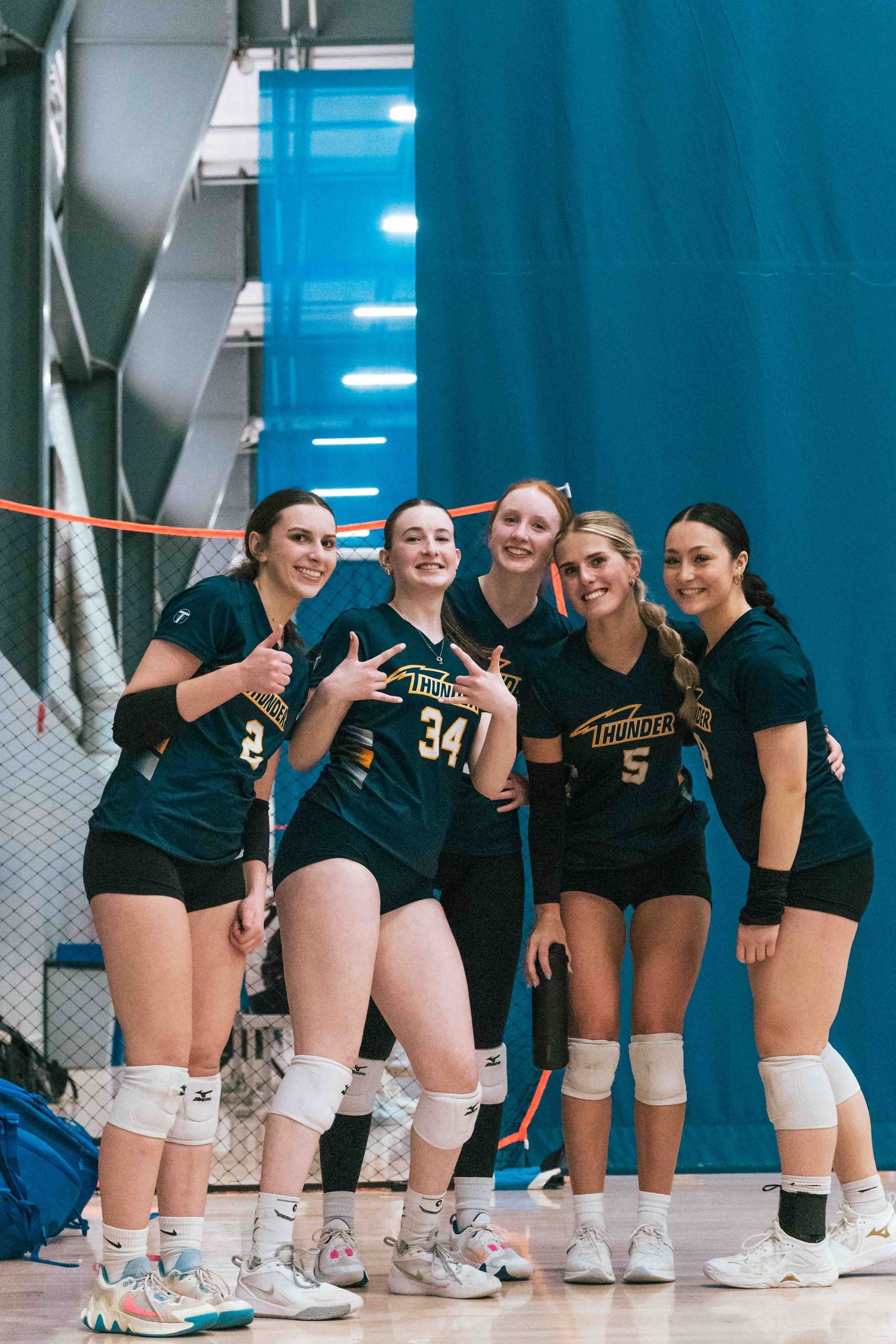 Volleyball team wearing dark green uniforms poses together against a blue backdrop.