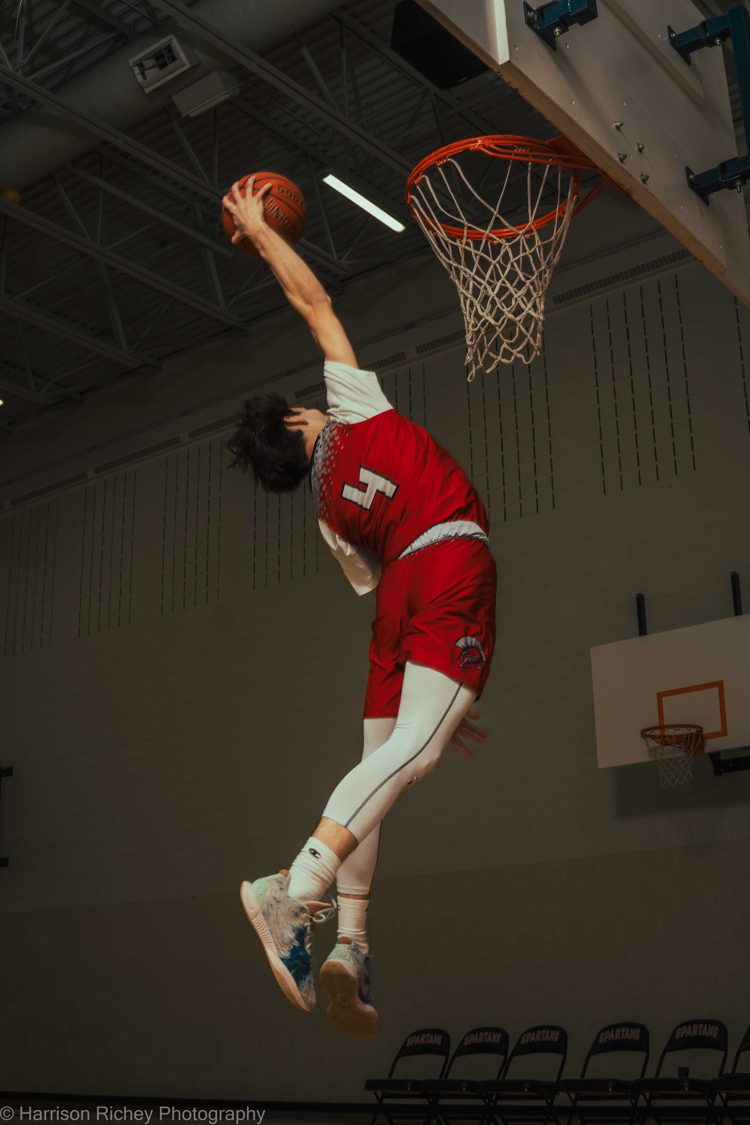 Basketball player in red uniform demonstrates impressive vertical leap during indoor practice session.