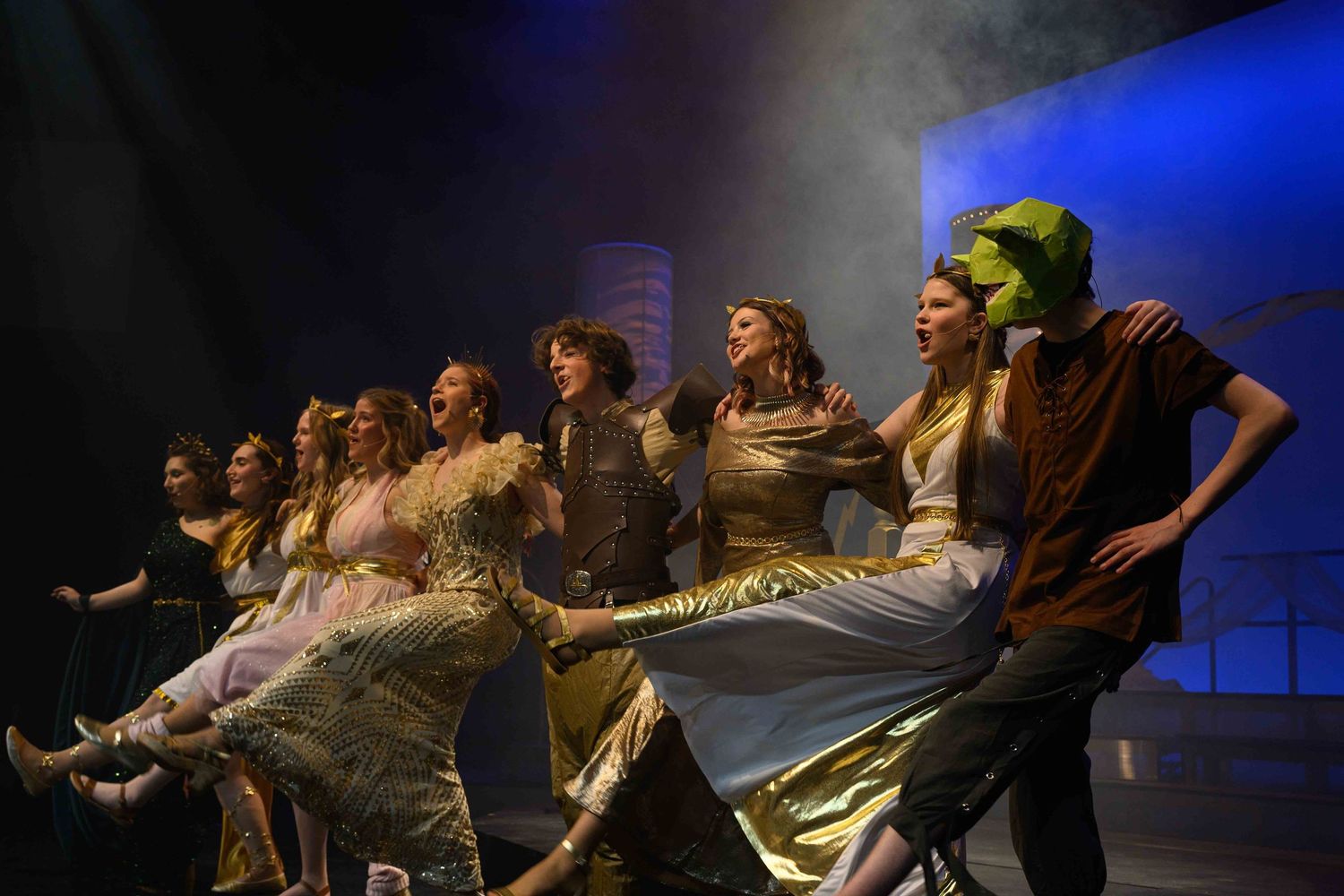 Performers in dark costumes on stage during a theatrical production with dramatic lighting.