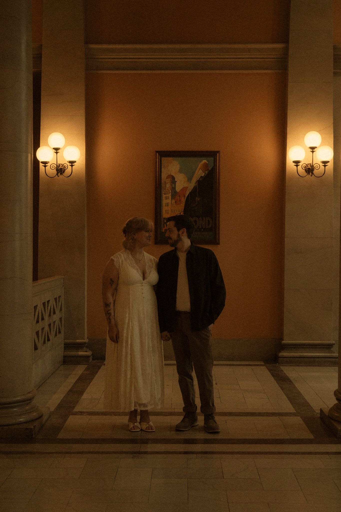 A couple in wedding attire dances together in a dimly lit hallway with wall sconces creating romantic ambiance.