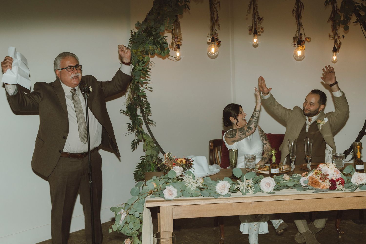 A group celebrates at an elegant wedding reception with string lights and greenery decorations.
