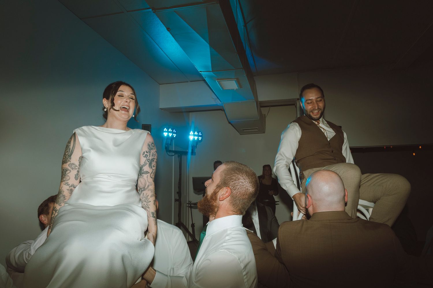 Wedding guests celebrate during the hora dance at a reception with blue lighting.