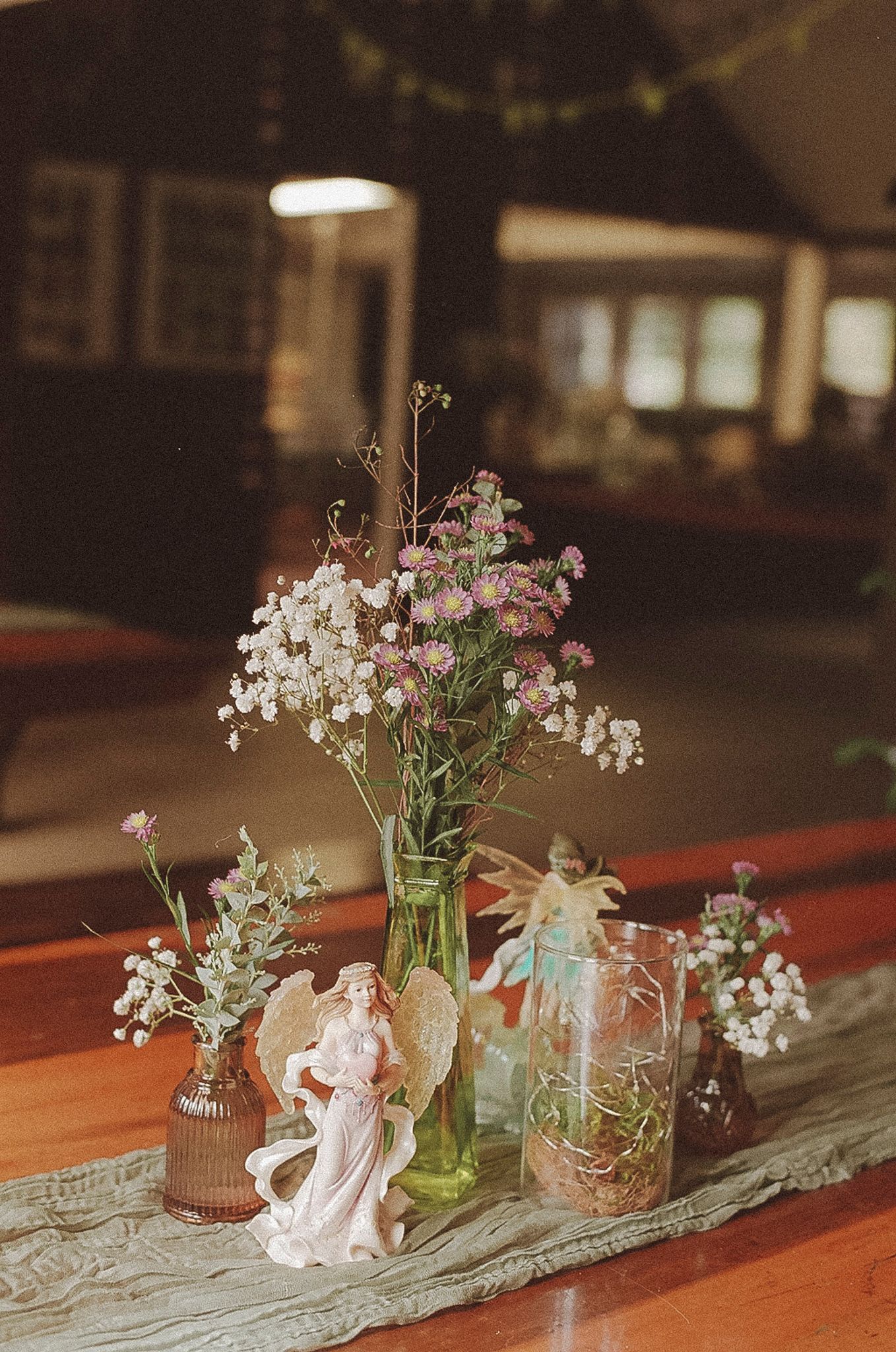 Delicate floral centerpieces with pink and white flowers in vintage glass vases arranged on a rustic wooden table.