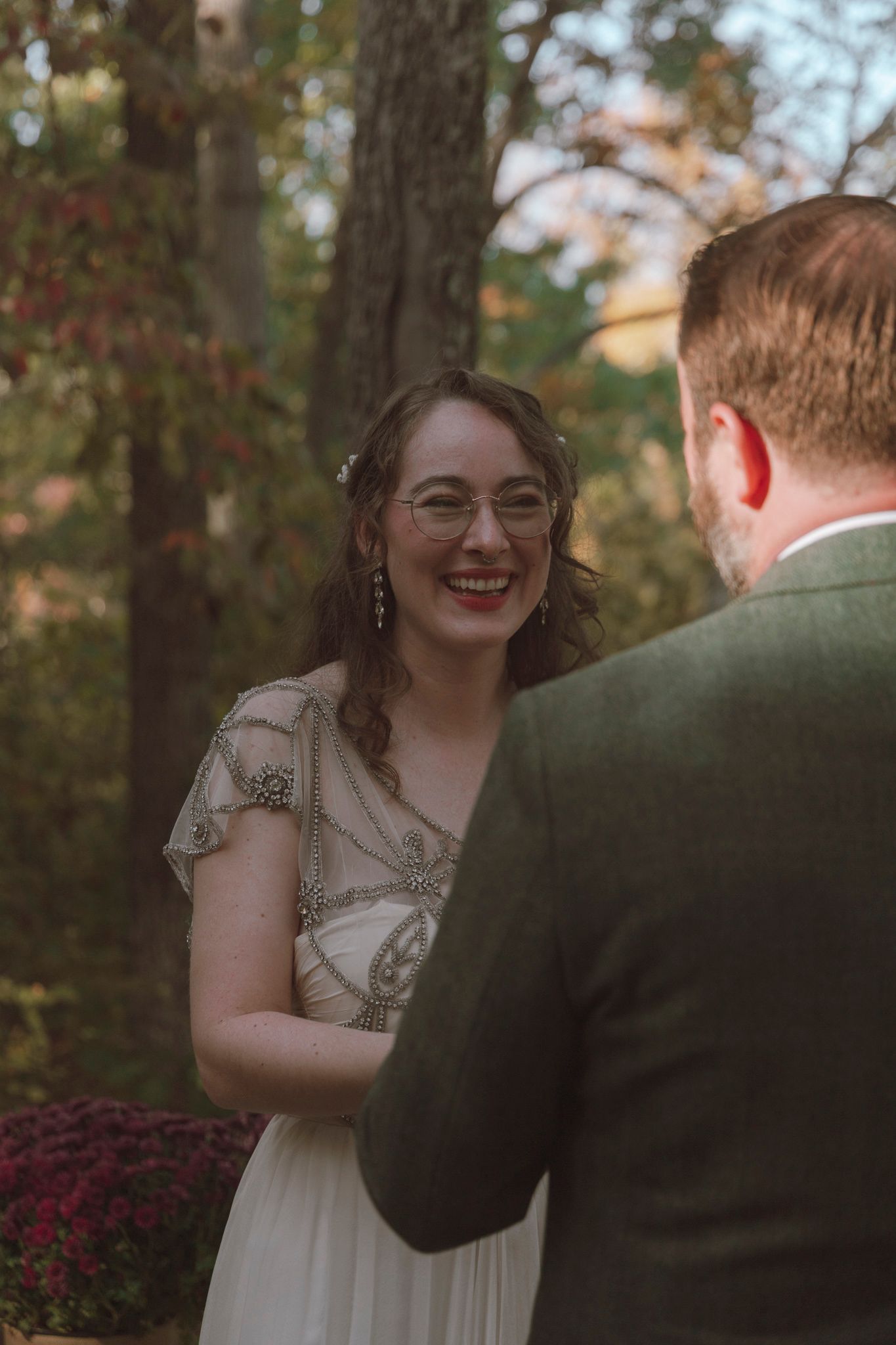 A joyful interaction between two people in a garden setting with autumn trees and burgundy flowers visible.