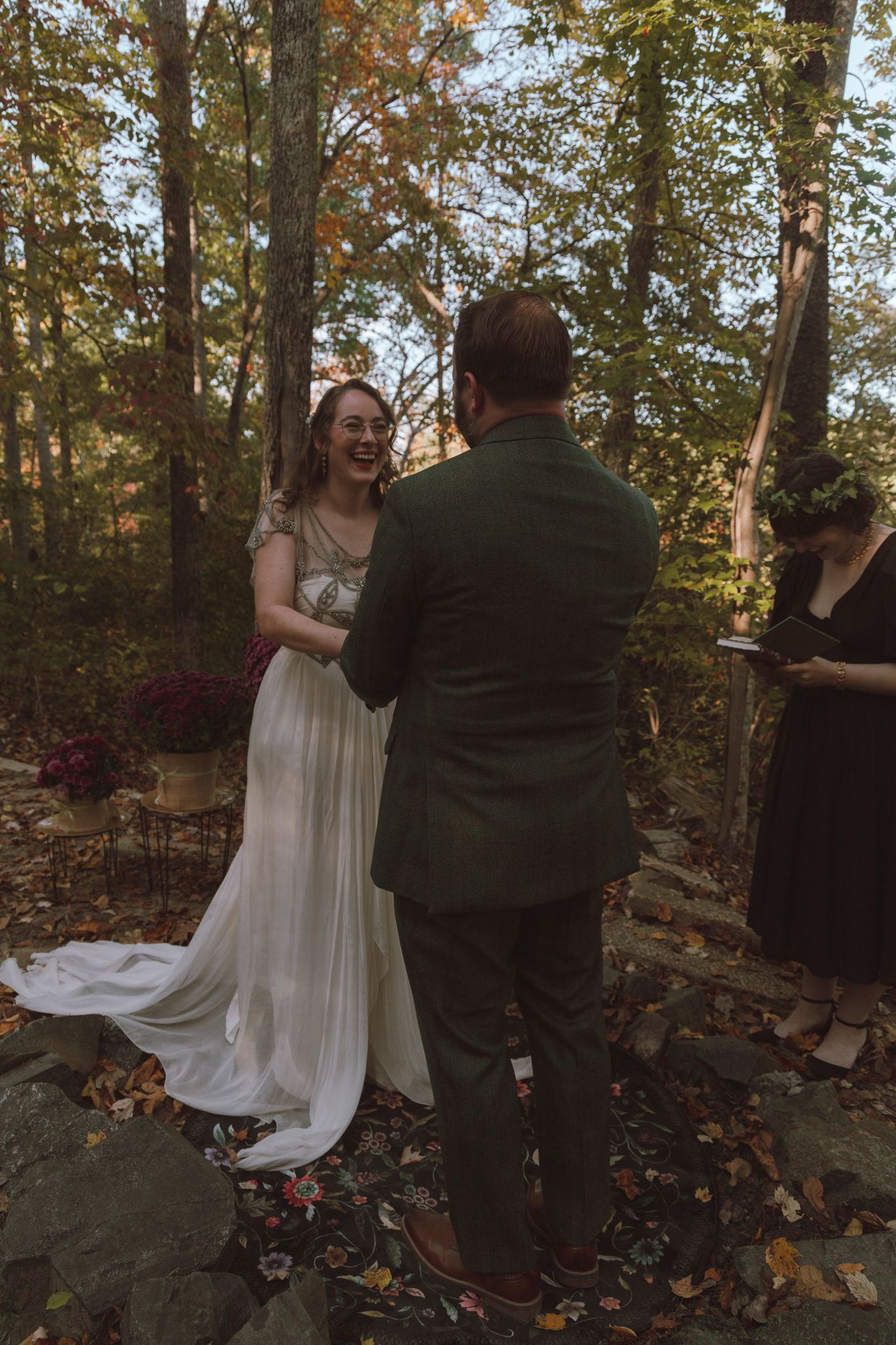 A couple shares a joyful moment during their autumn forest wedding ceremony as fallen leaves cover the ground.