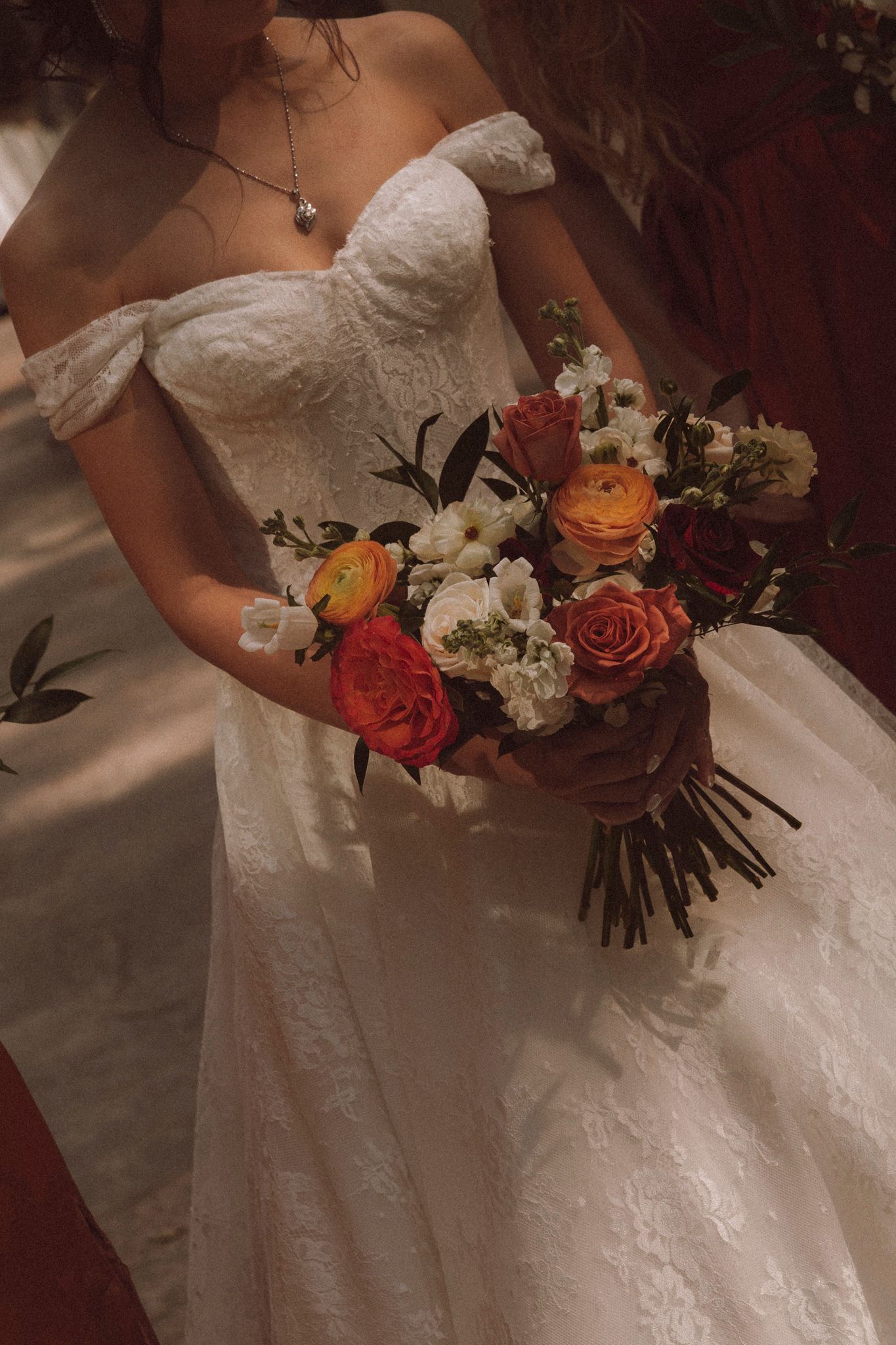 A close-up view of a bridal bouquet featuring coral roses and white flowers against a lace wedding dress.
