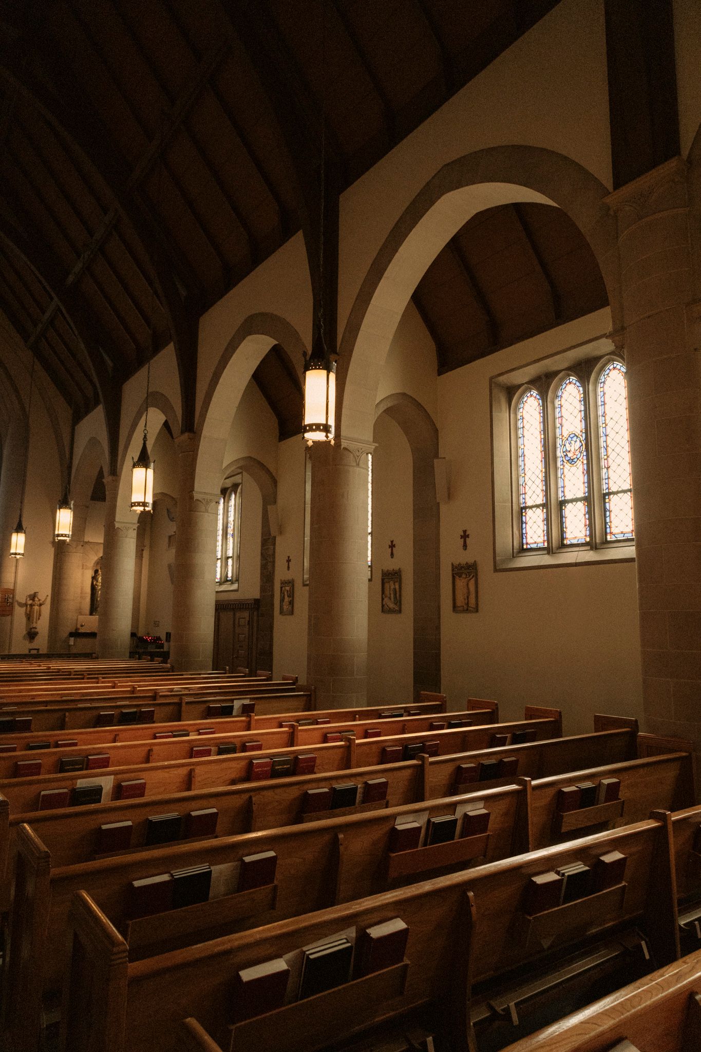 Interior of a traditional church featuring wooden pews, arched ceilings, hanging lanterns, and stained glass windows.
