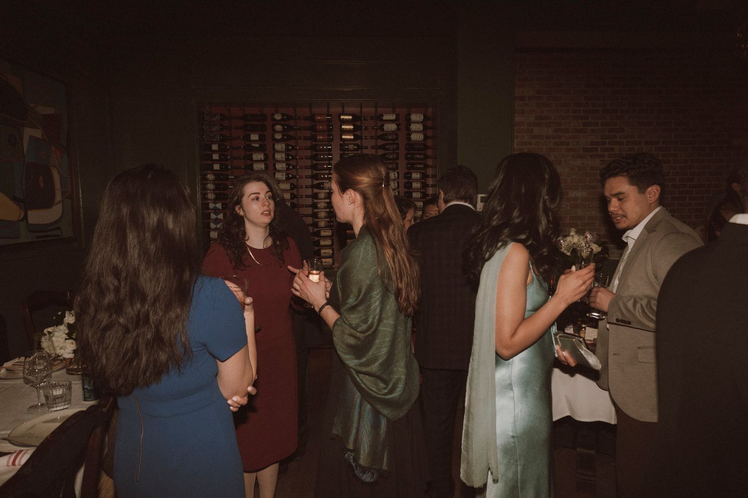 Guests mingling at an elegant indoor evening event, with women in formal dresses conversing in a dimly lit venue.