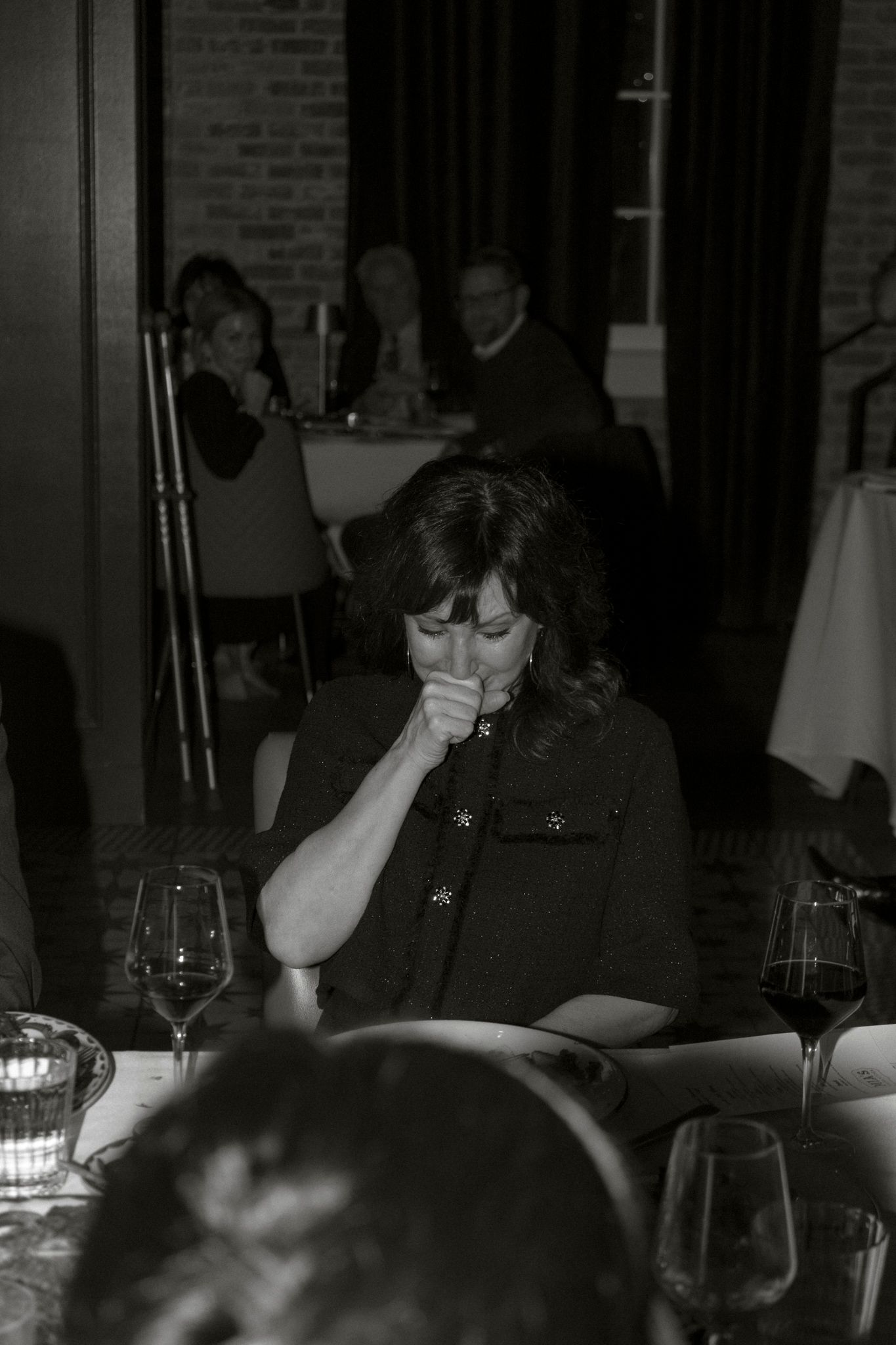 Emotional woman covering mouth at wedding reception table in black and white photography.