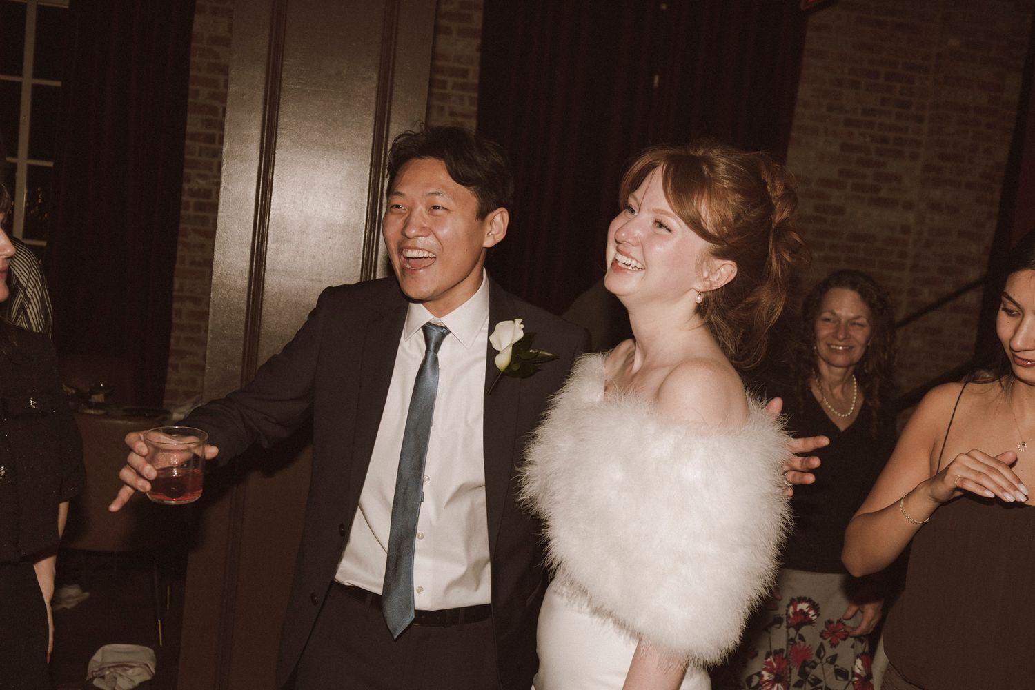 Joyful newlywed couple dancing together at wedding reception, bride wearing white feather wrap.