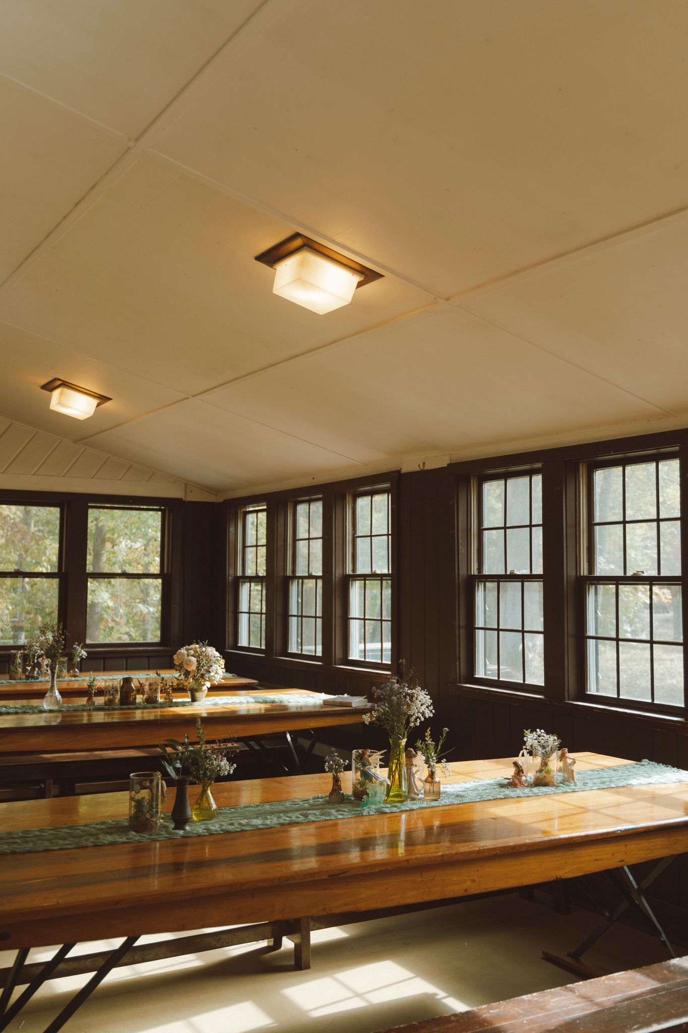 Long wooden benches line the interior of a rustic dining hall with windows letting in natural light.