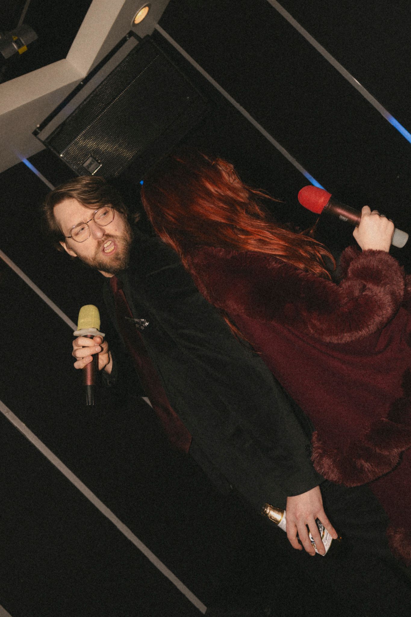 Person with long red hair wearing black clothing dancing in a dark room with dramatic lighting.