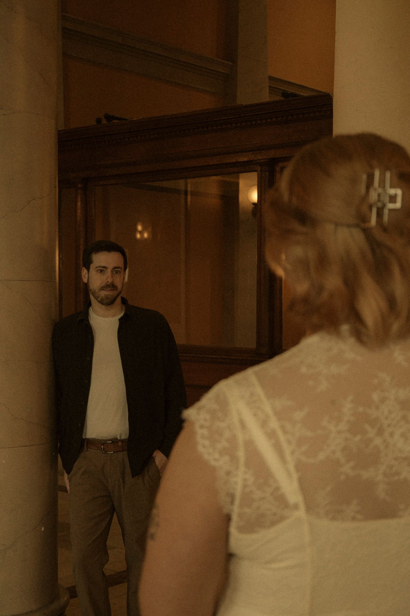 A couple in wedding attire walking through an elegant indoor venue with pillars.