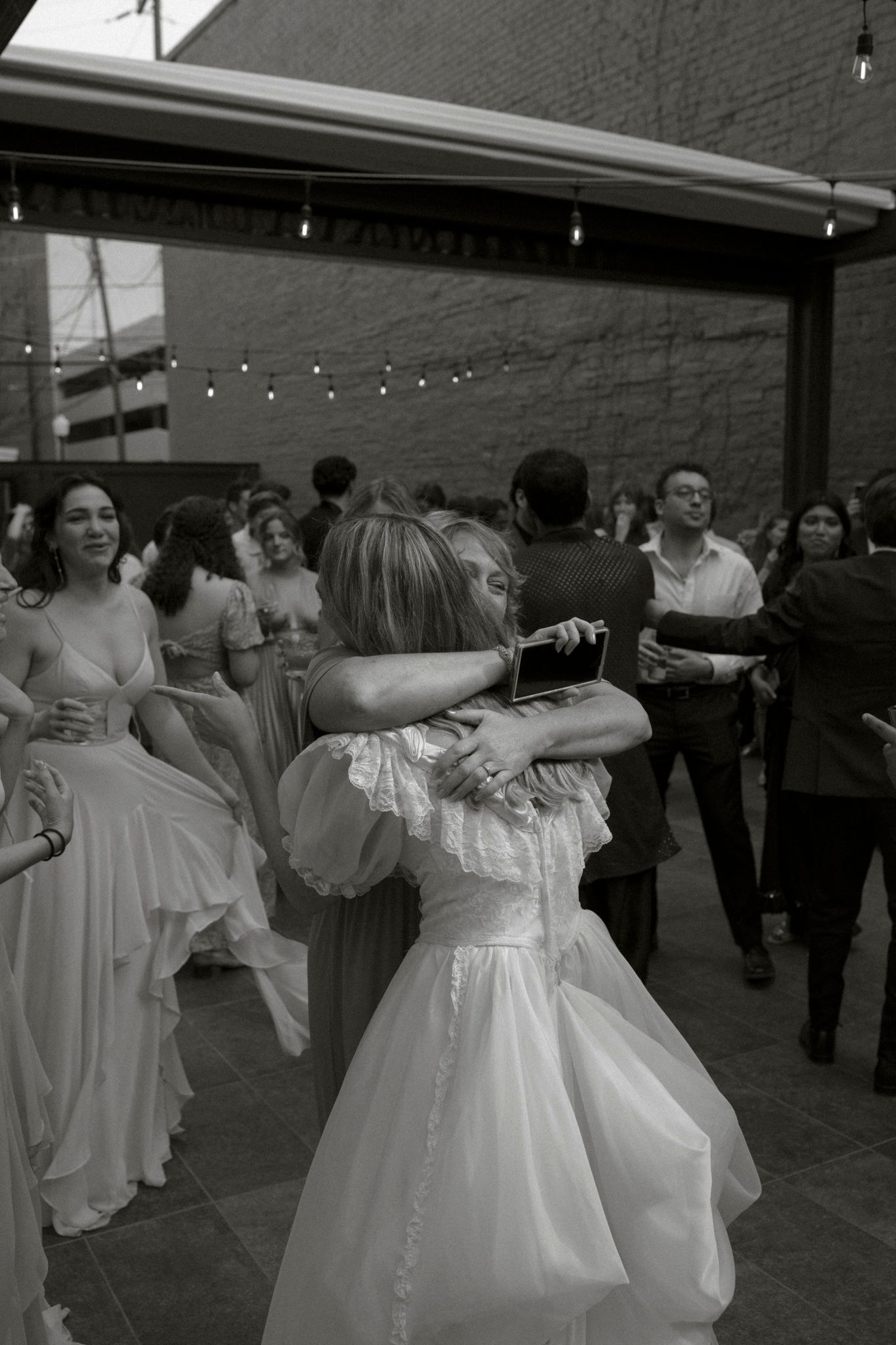 Black and white photo of people dancing at a wedding reception under string lights on an outdoor patio.
