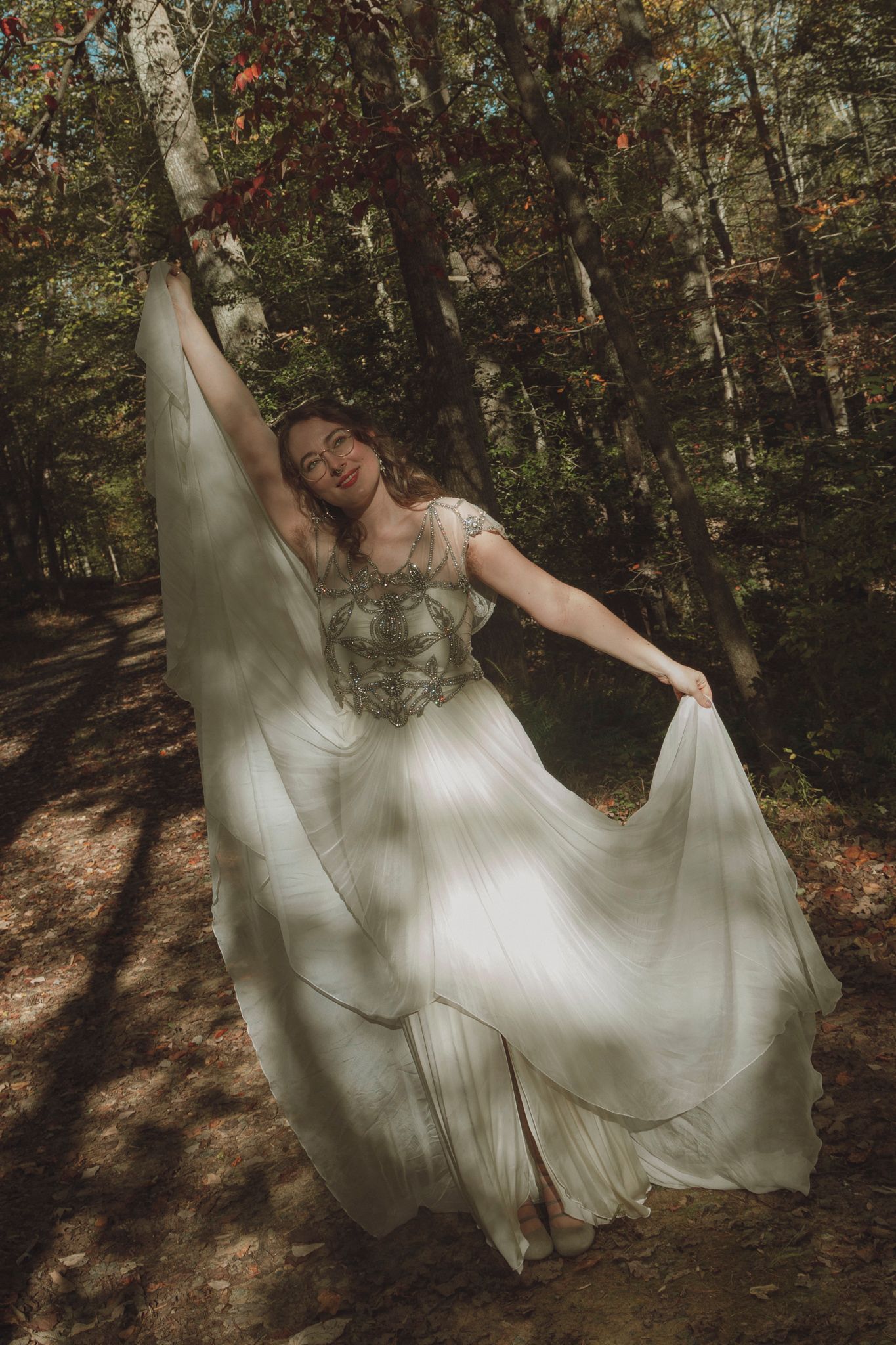 A flowing white wedding dress twirls gracefully through a sunlit autumn forest setting.