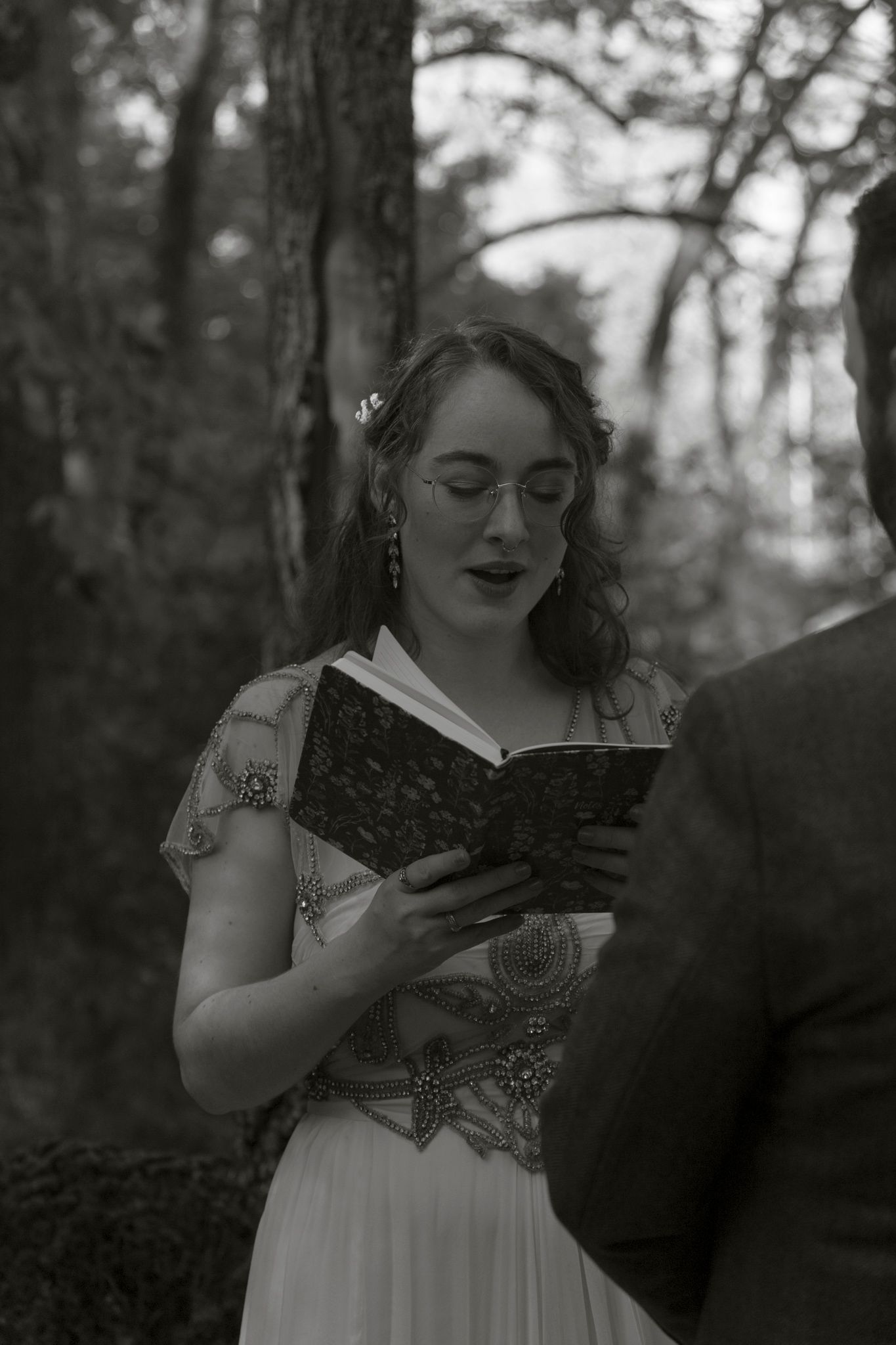 A series of black and white photos showing someone in a white dress reading a book in a forest setting.