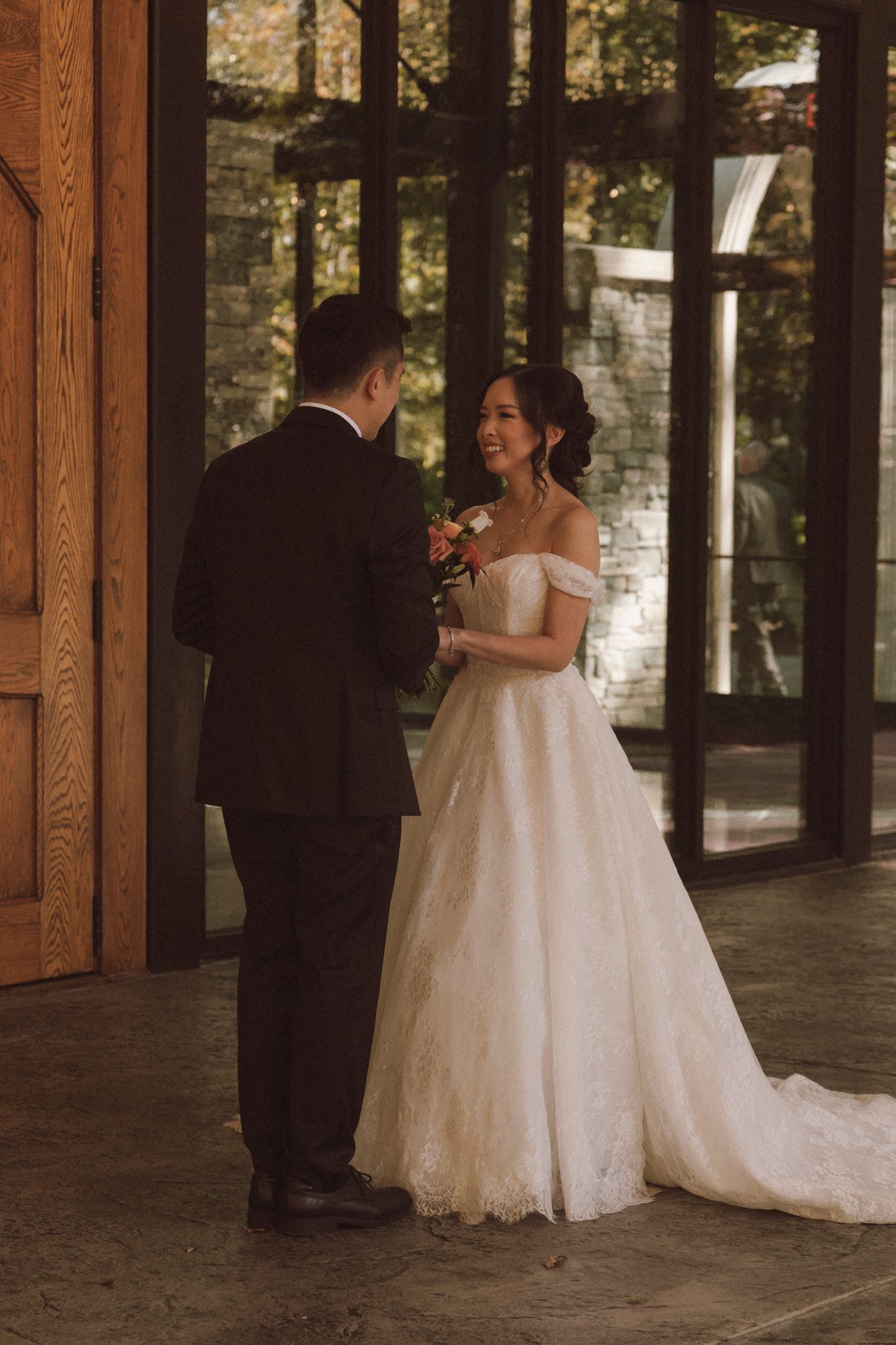 A tender moment between newlyweds sharing laughter in an elegant venue with wooden doors and stone walls.