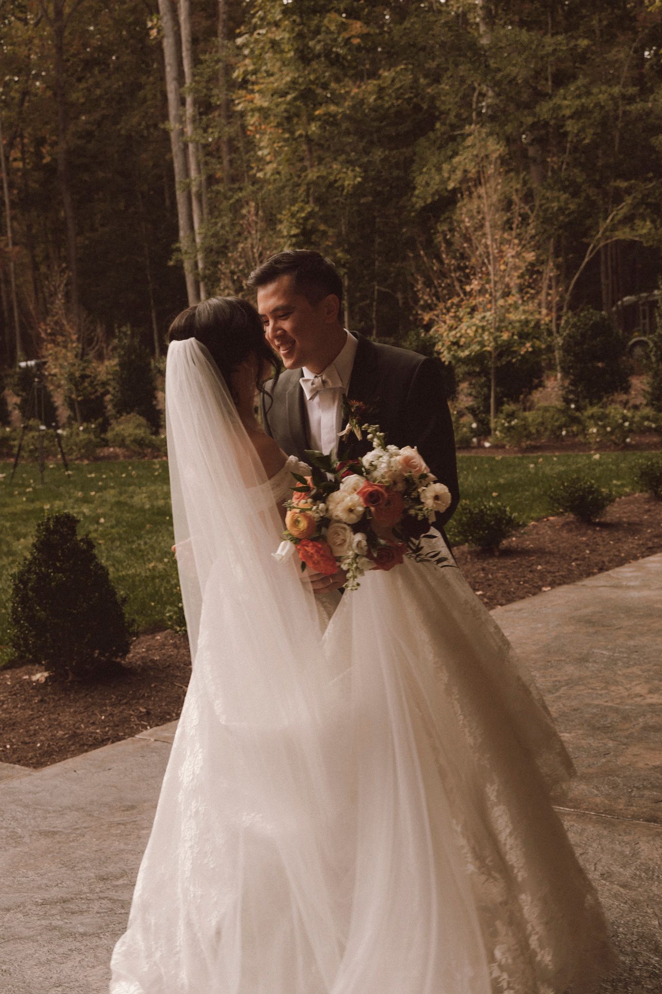 A bride and groom share a romantic moment on a stone pathway surrounded by autumn trees and greenery.