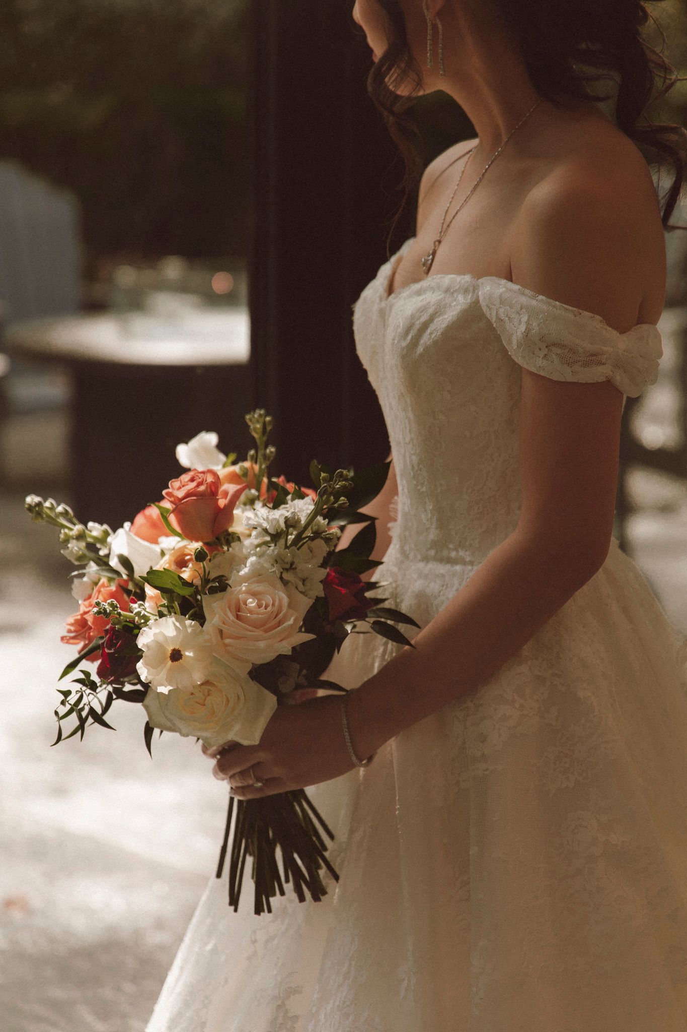 A bride in a white off-shoulder wedding dress holds a romantic bouquet of pink roses and white flowers.
