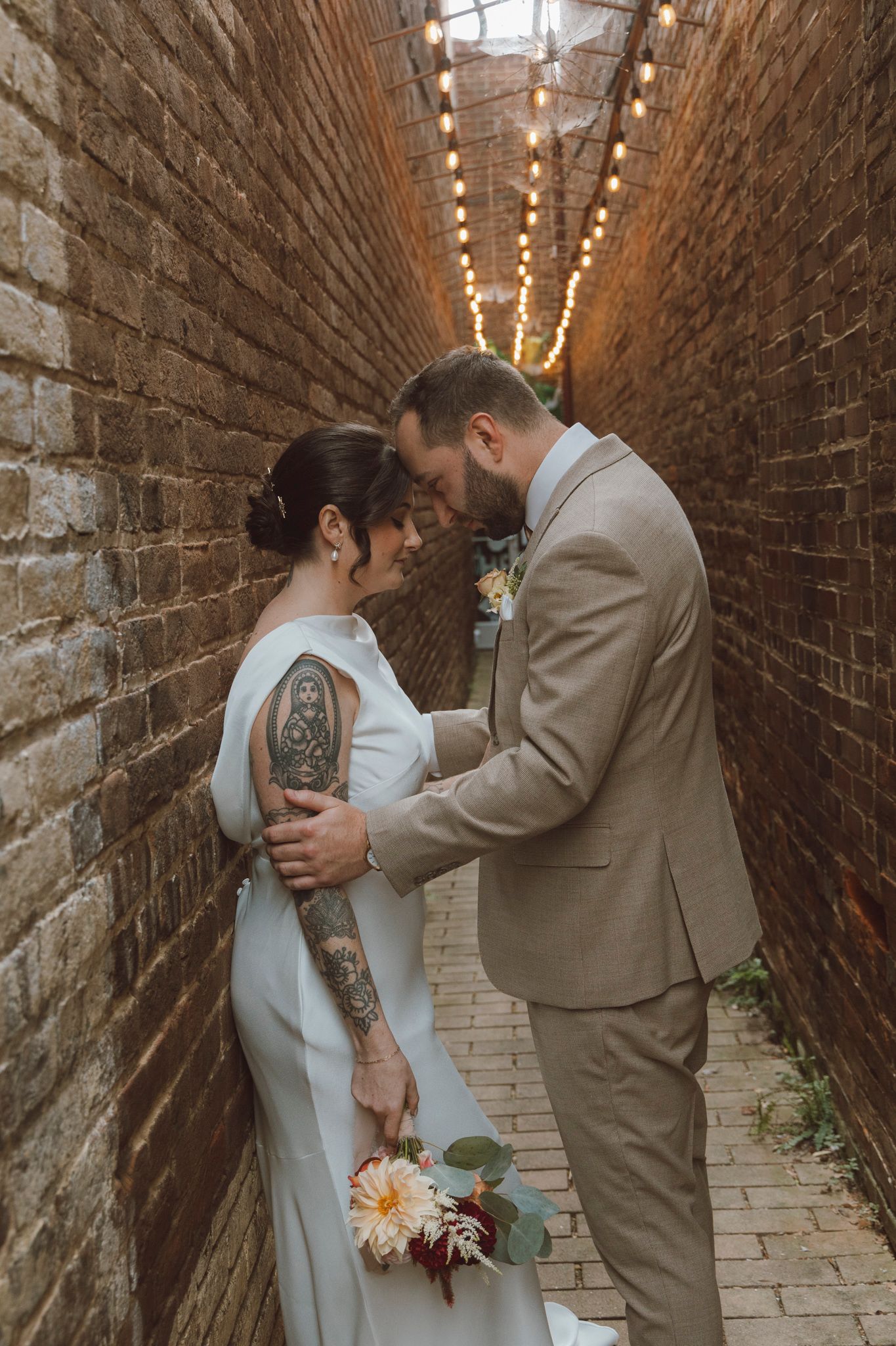 Romantic wedding photos captured in a brick-lined alley with string lights overhead.