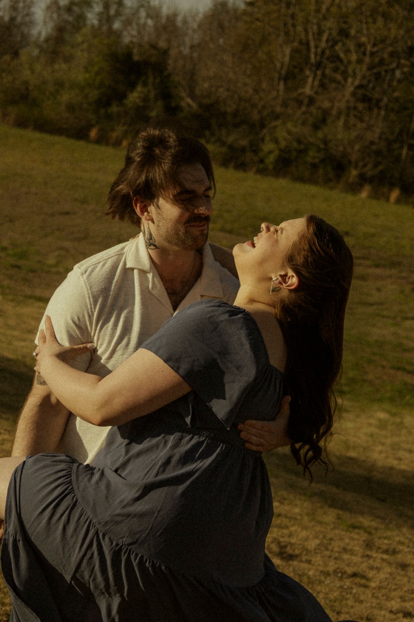 Romantic couple embracing and laughing together in a sunny outdoor field.
