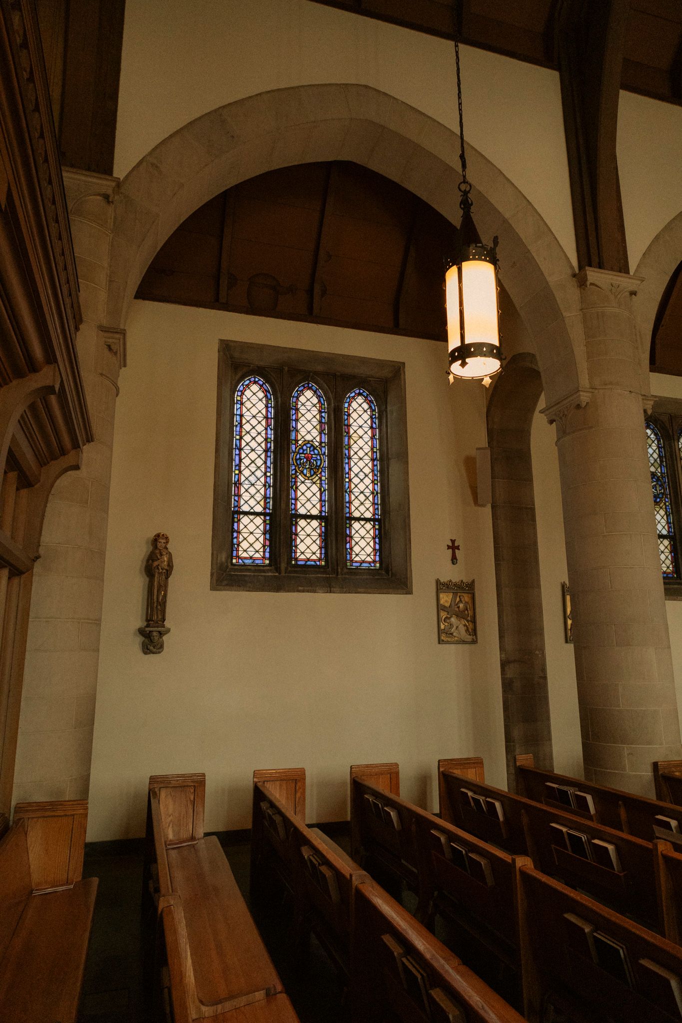 Interior of a historic church featuring wooden pews, stone arches, stained glass windows, and a hanging lantern.