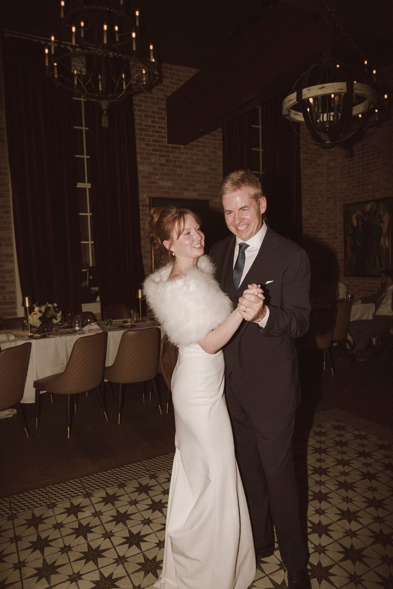 Bride and groom share romantic first dance in elegant venue with chandelier lighting.
