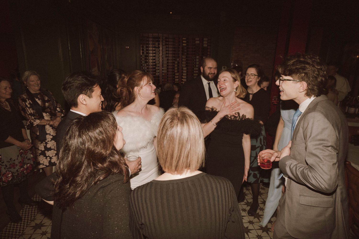 Wedding guests laughing and socializing together on the dance floor at a festive indoor reception.