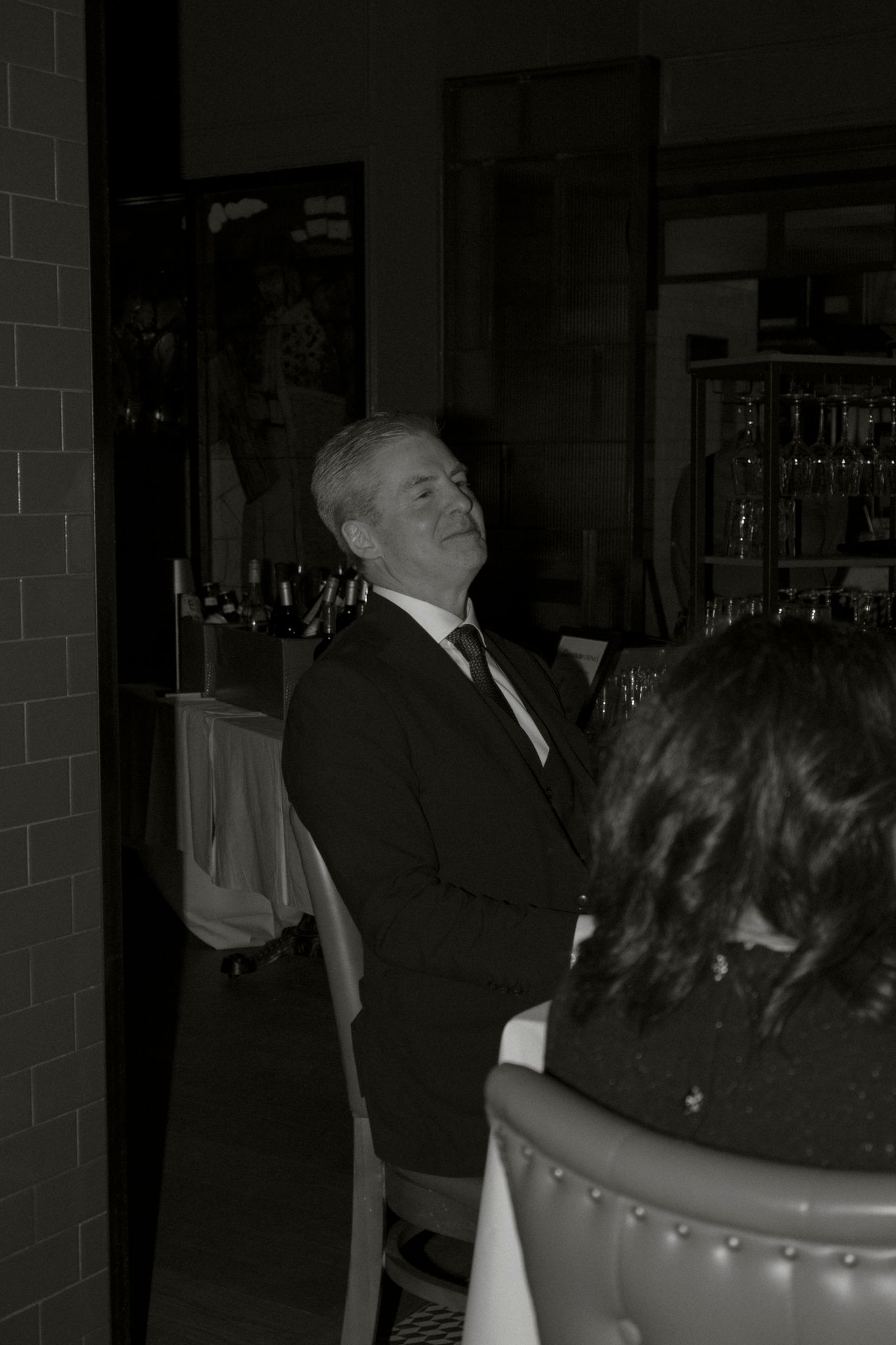 Man in dark suit smiling and laughing during a wedding reception in black and white photo.